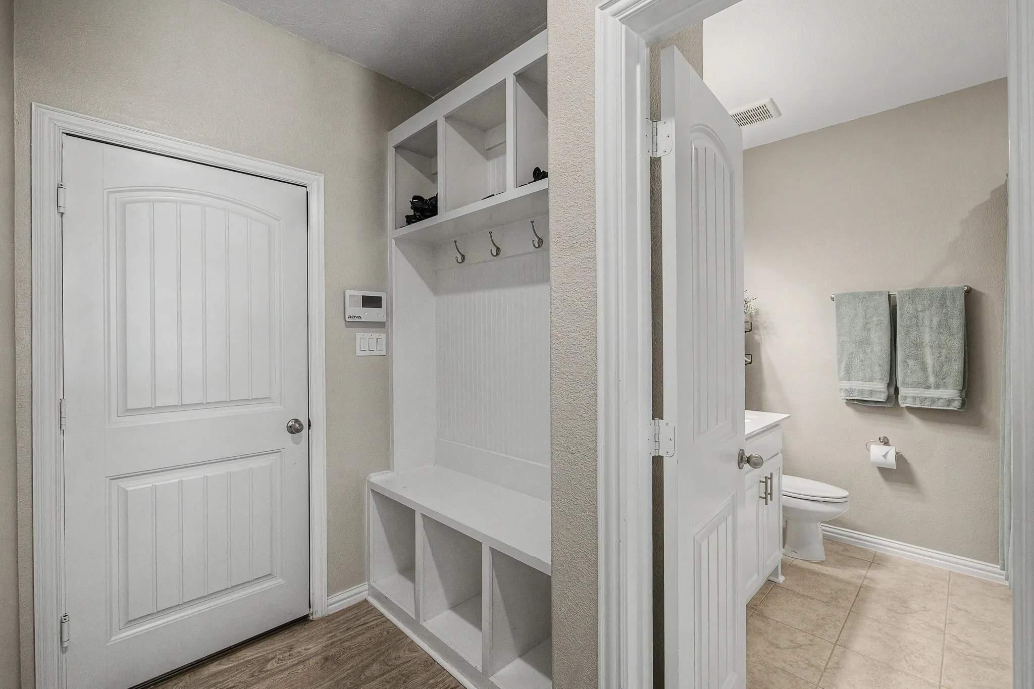 Built-in hall tree with storage cubbies and coat hooks, wood-finish flooring, and a white paneled door