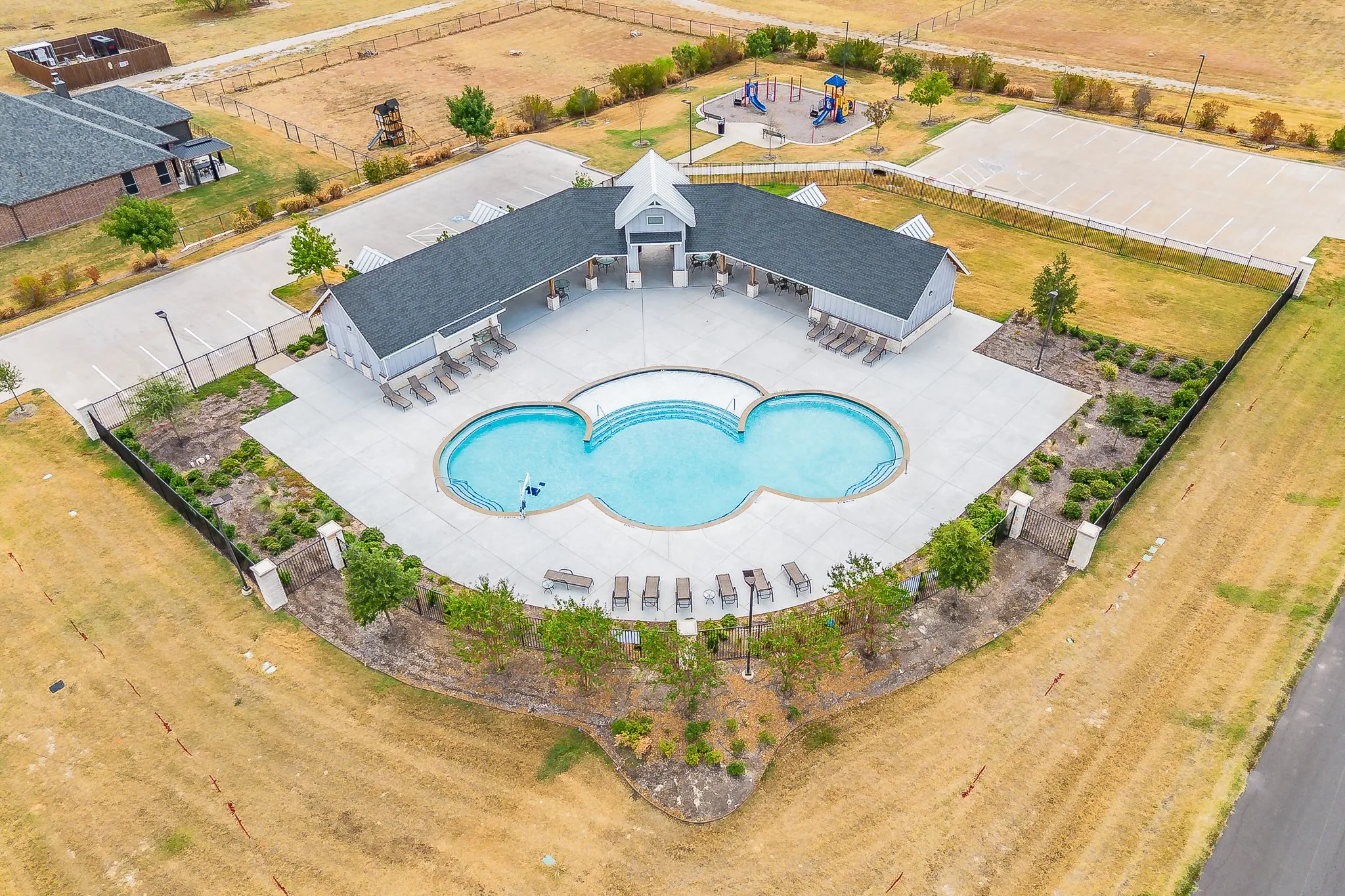 Community pool with multiple lounge chairs, surrounding paved deck, and adjacent covered seating areas