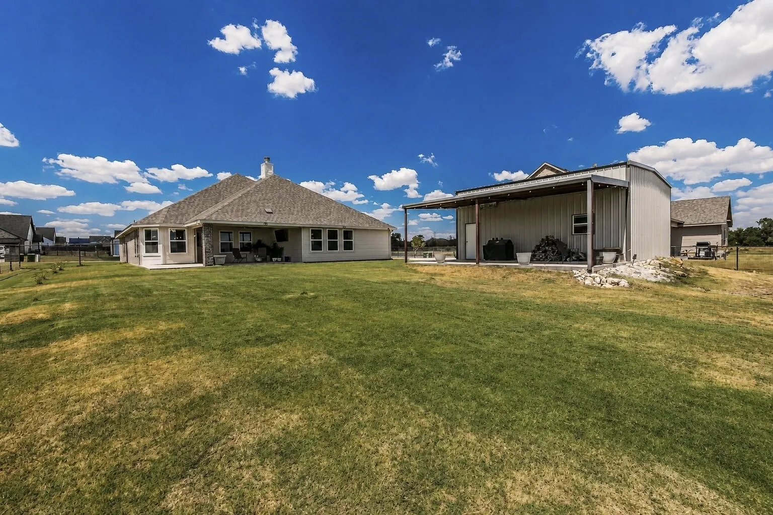 Expansive yard with a single-story residence and a separate outbuilding featuring a covered patio