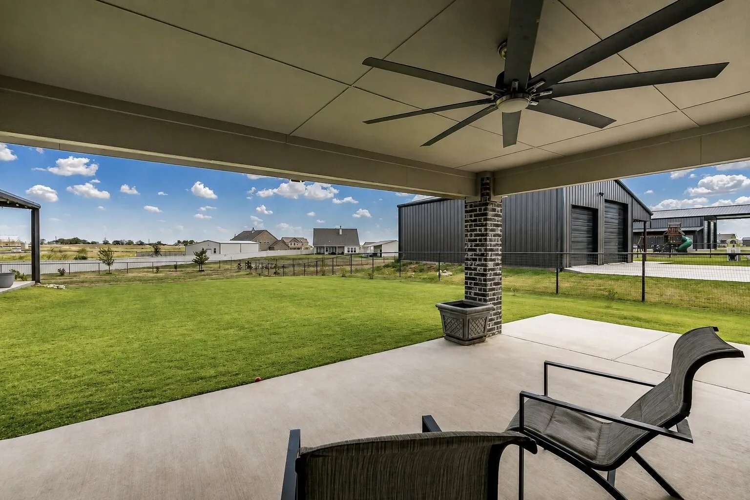 Expansive covered patio with a large ceiling fan, concrete flooring, and a brick-clad support column