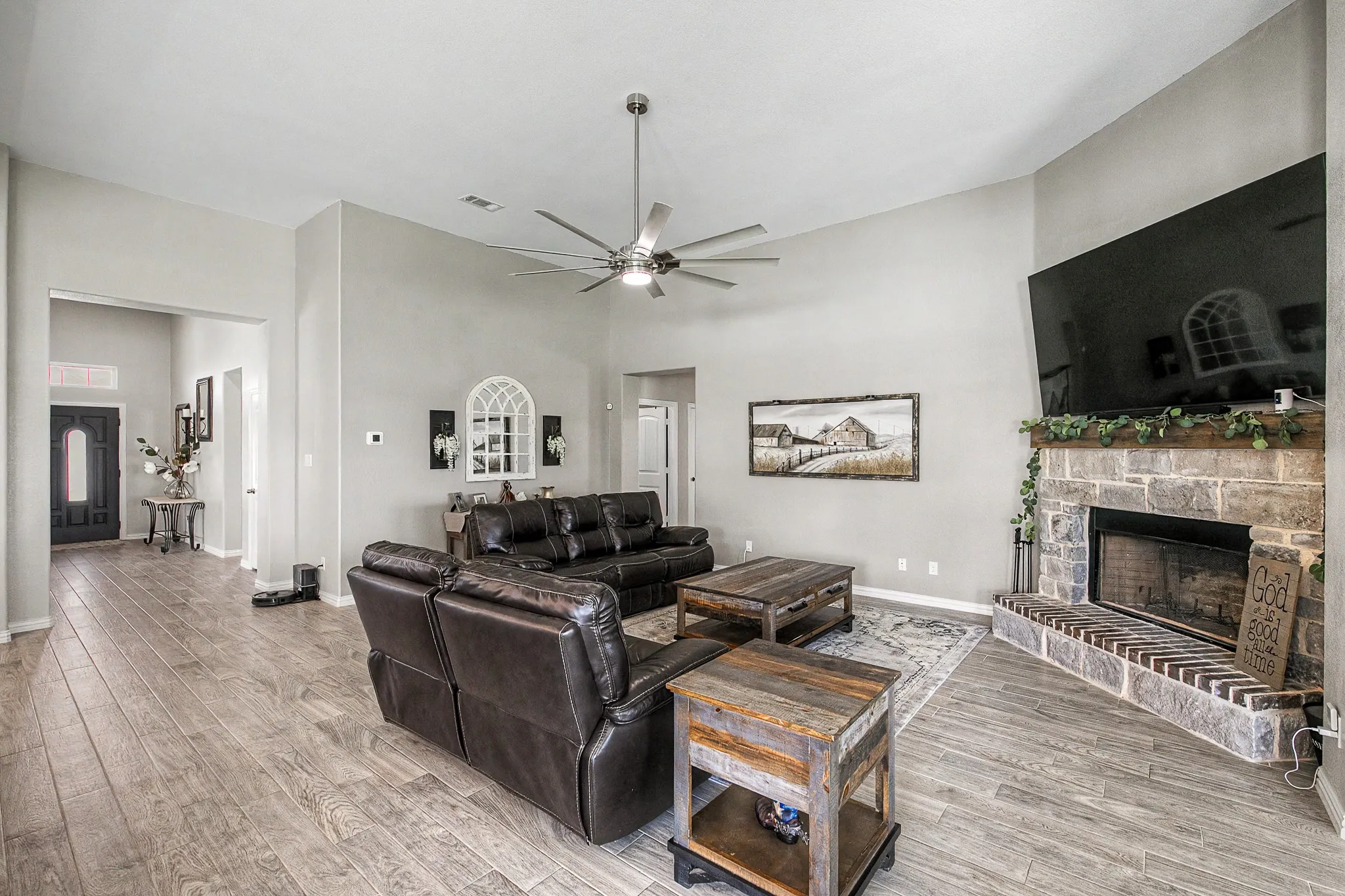 Vaulted ceilings, wood-finish flooring, stone-clad fireplace with a hearth, and a ceiling fan with integrated lighting