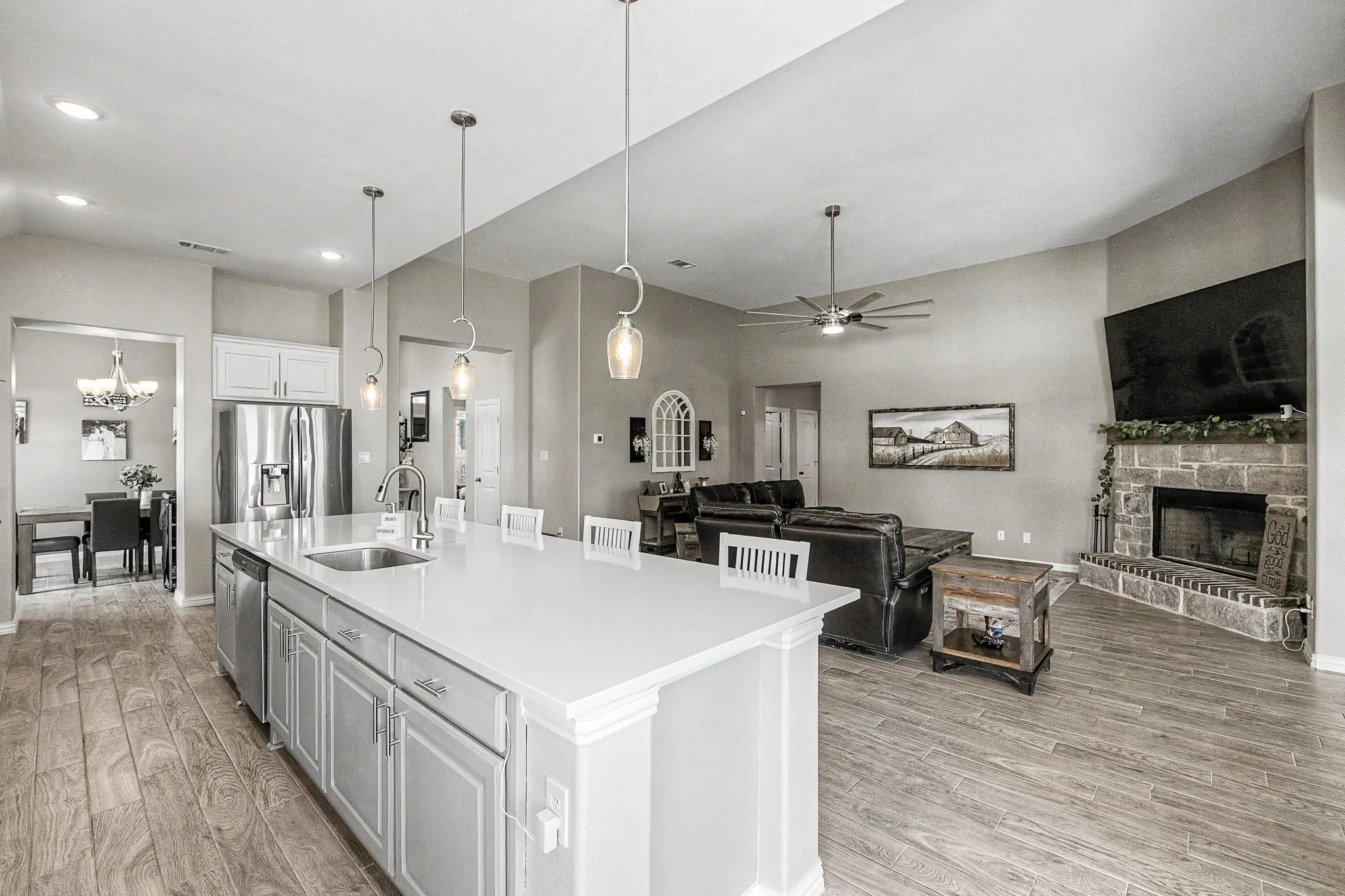 Spacious kitchen island with an undermount sink, stainless steel appliances, wood-finish flooring, a stone-faced fireplace, and high ceilings