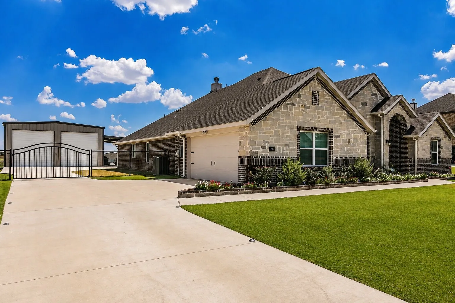 Stone and brick exterior with a two-car garage, manicured lawn, and a separate two-bay outbuilding with a private gated entrance