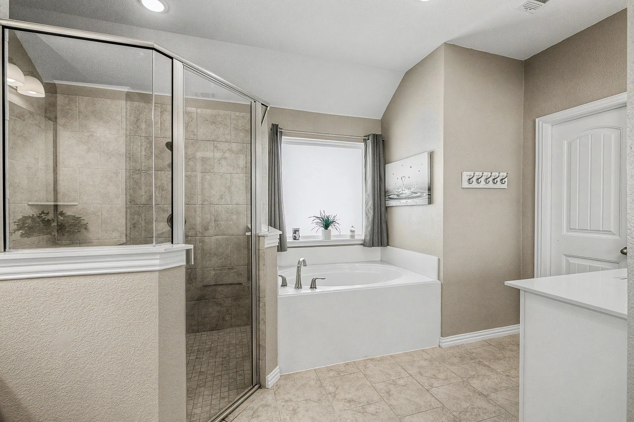 Bathroom featuring a tiled walk-in shower with glass enclosure, a built-in soaking tub, and a vanity with a light-colored countertop