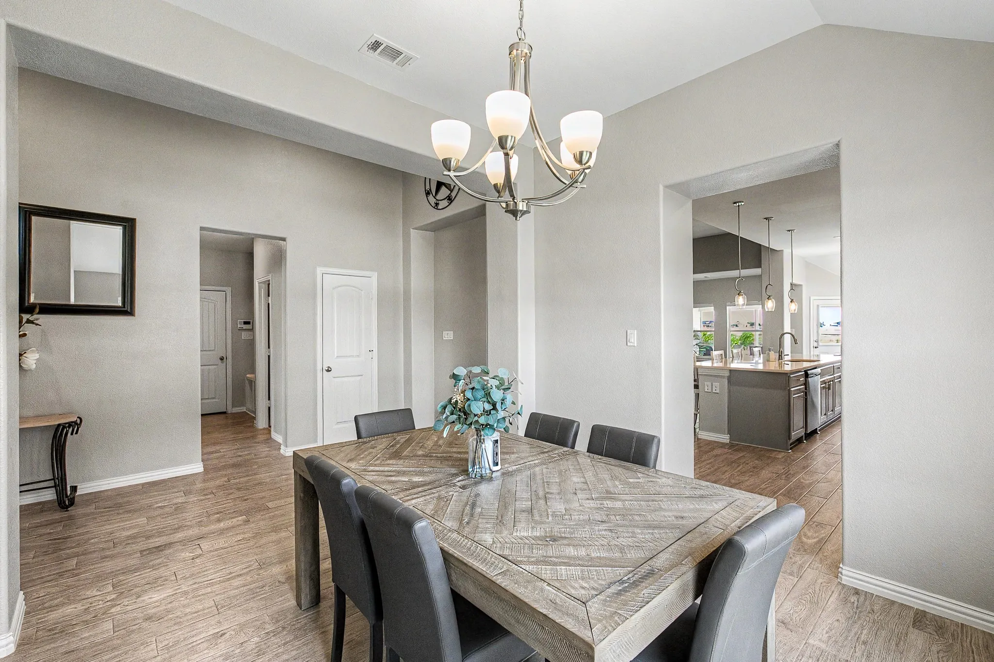 Vaulted ceilings, wood-finish flooring, and a brushed nickel chandelier with frosted glass shades