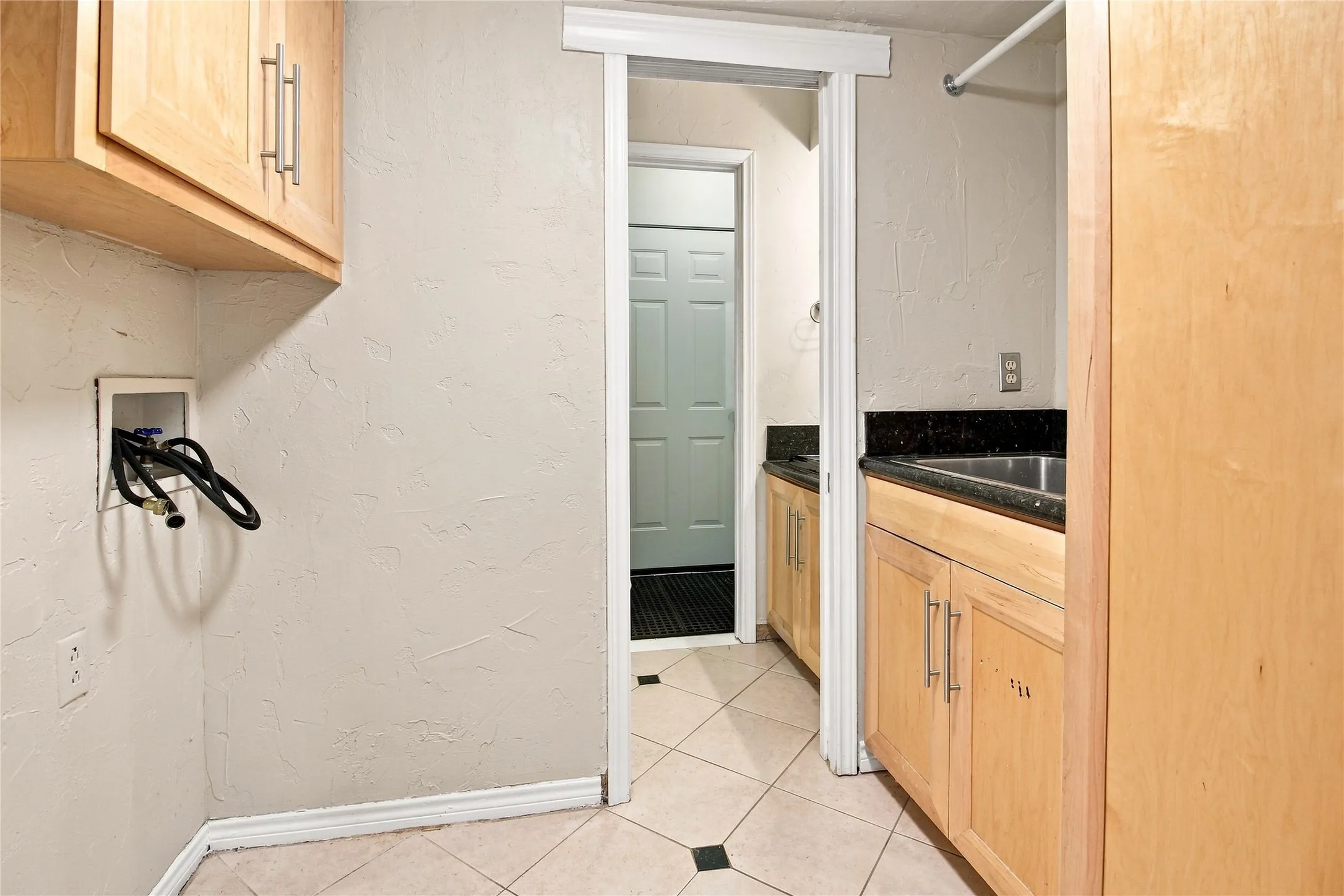 Light wood-finish cabinetry, stainless steel sink, dark stone-finish countertop, and tiled flooring