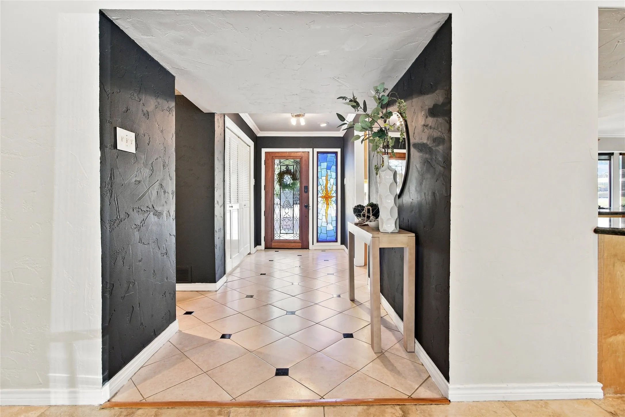 Entryway featuring tile flooring with dark accent tiles, a wood-panel front door with glass inserts, and a stained-glass sidelight