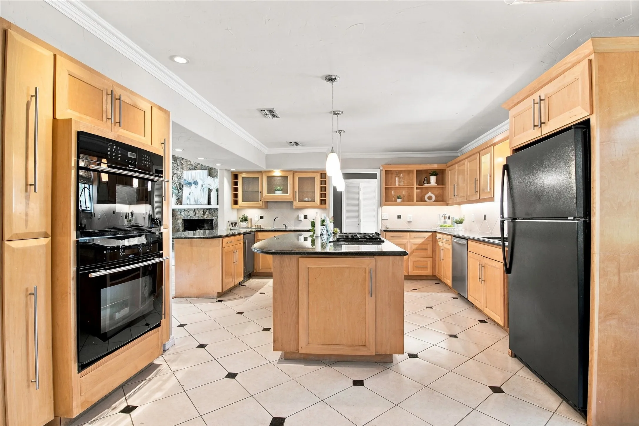 Kitchen featuring light wood cabinetry, black appliances, a central island with a cooktop, pendant lighting, and tile flooring