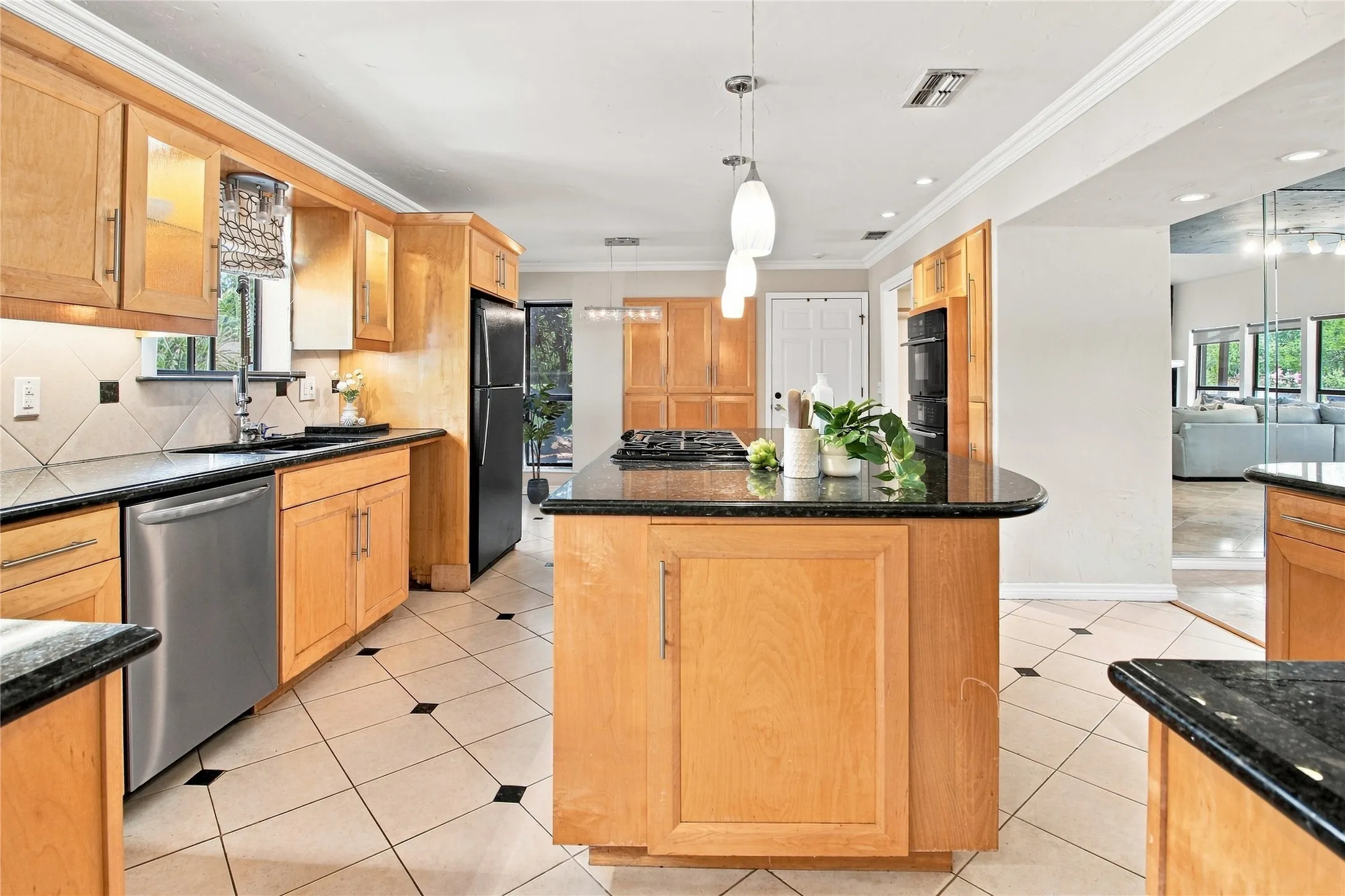 Kitchen featuring light wood cabinetry, dark countertops, built-in stainless steel appliances, and a central island with an integrated cooktop