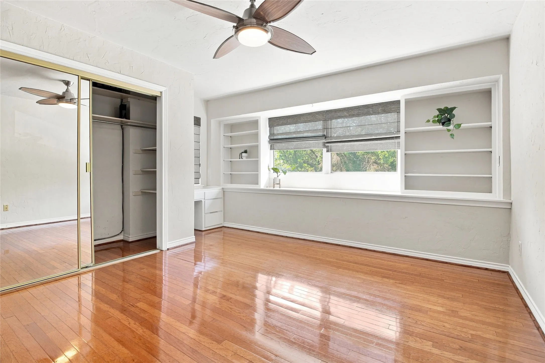 Hardwood flooring bedroom, mirrored closet doors, built-in shelving, built-in desk, and a ceiling fan with integrated lighting