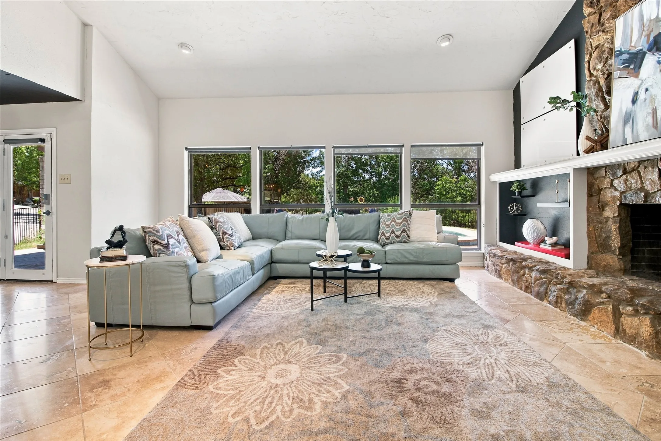 Vaulted ceiling, stone-clad fireplace with mantel, built-in shelving, tile flooring, and multiple windows