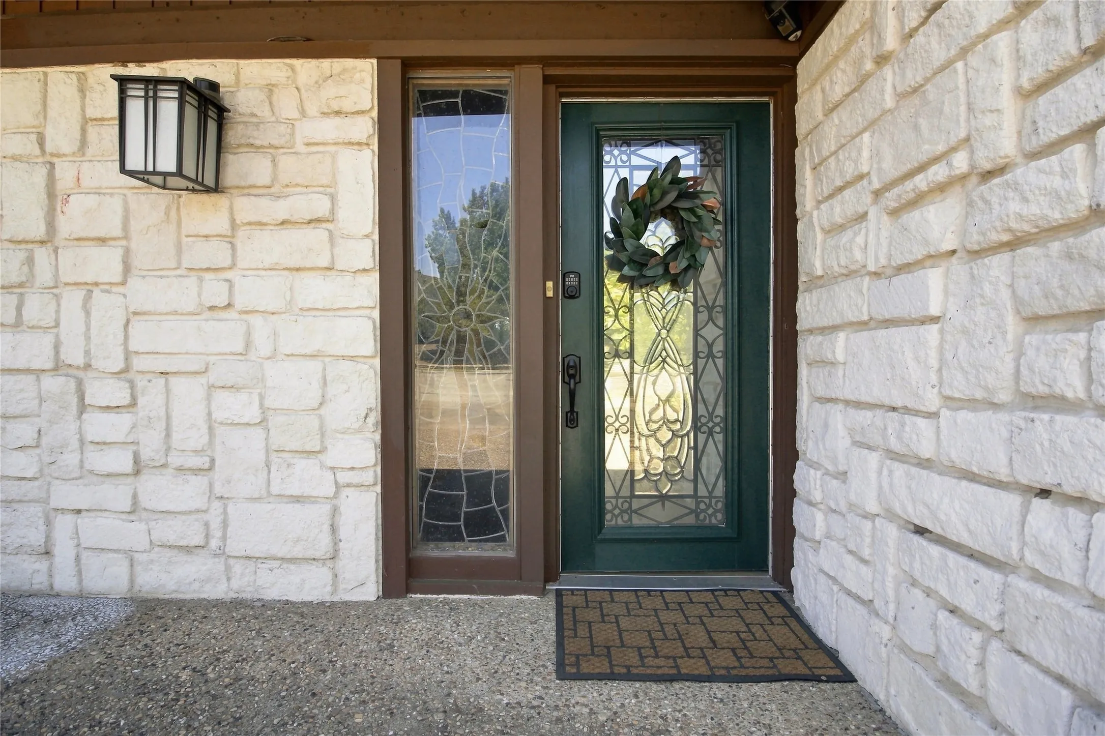 Stone-clad exterior with an ornate glass-paneled front door, an adjacent sidelight, and an exterior wall lantern