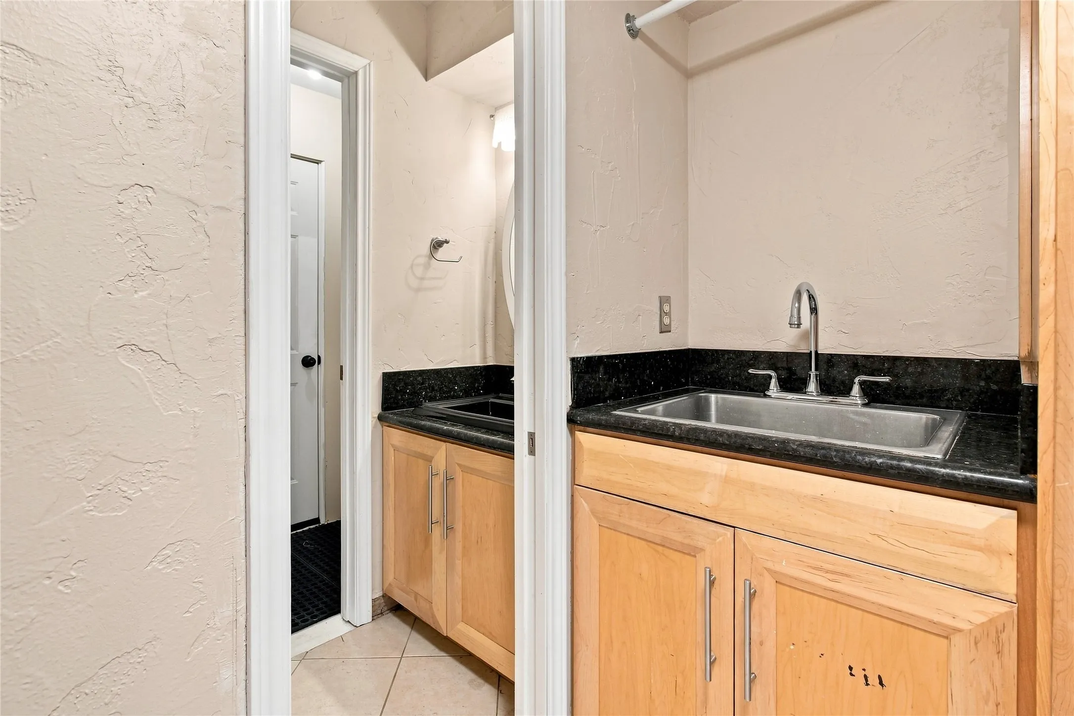 Half bath with light-toned wood cabinetry with brushed nickel hardware, dark stone countertop, and stainless steel undermount sink with chrome faucet