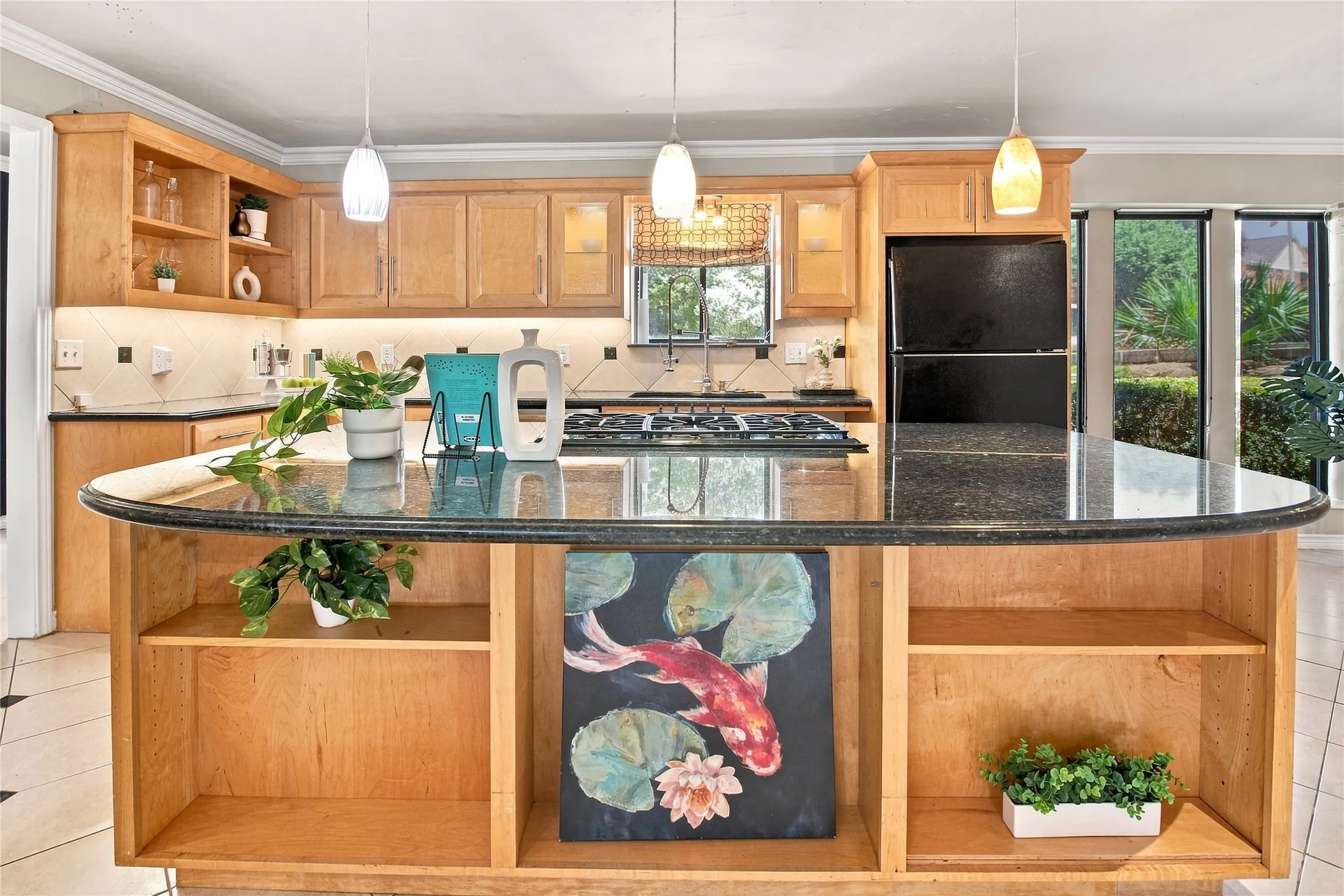 Kitchen featuring light wood cabinetry, a dark granite-style island with built-in shelving, a gas range, and a black refrigerator