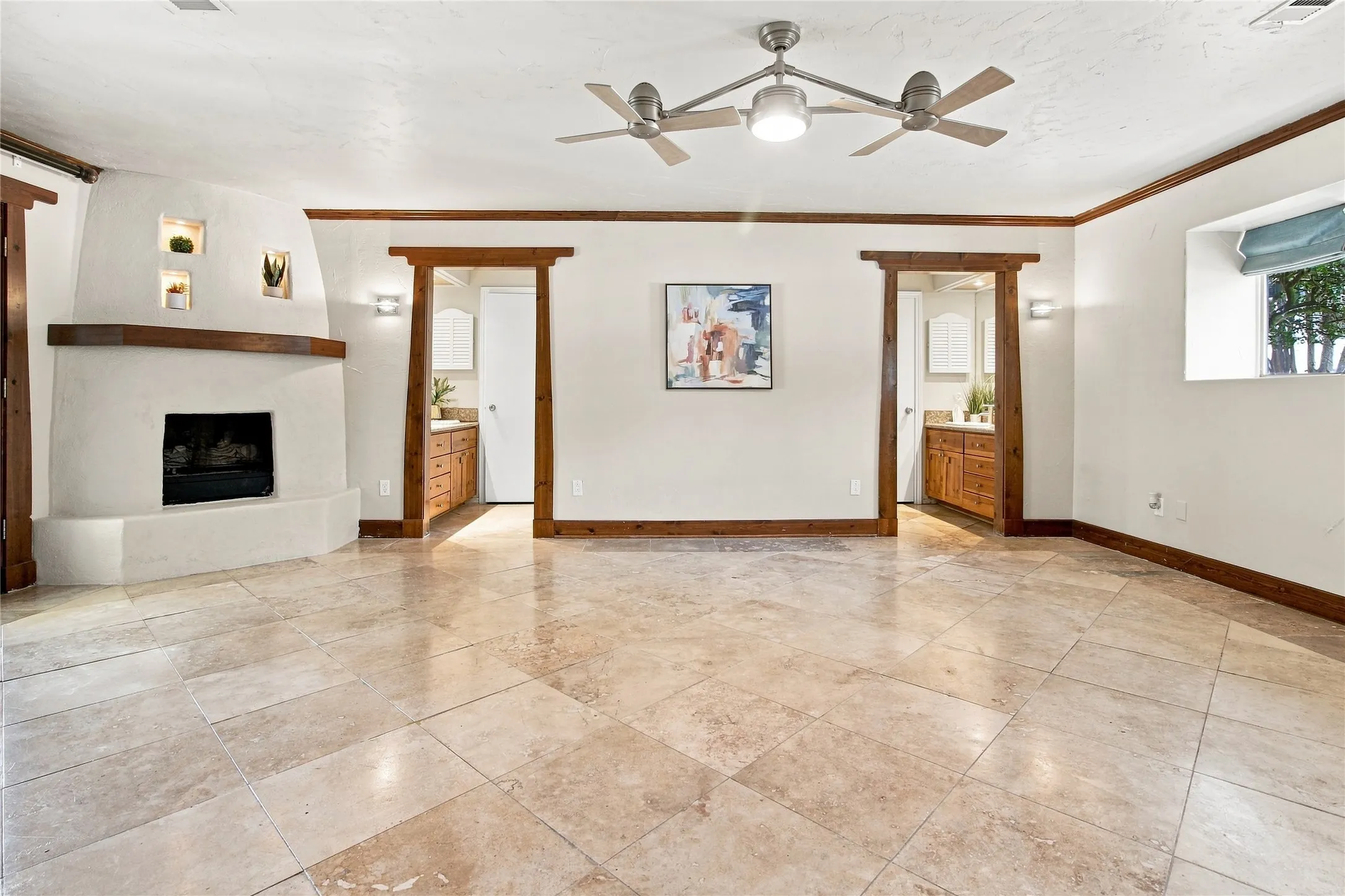 Primary bedroom with tile flooring, built-in fireplace, exposed wood trim, recessed wall niches, and dual ceiling fans with integrated lighting