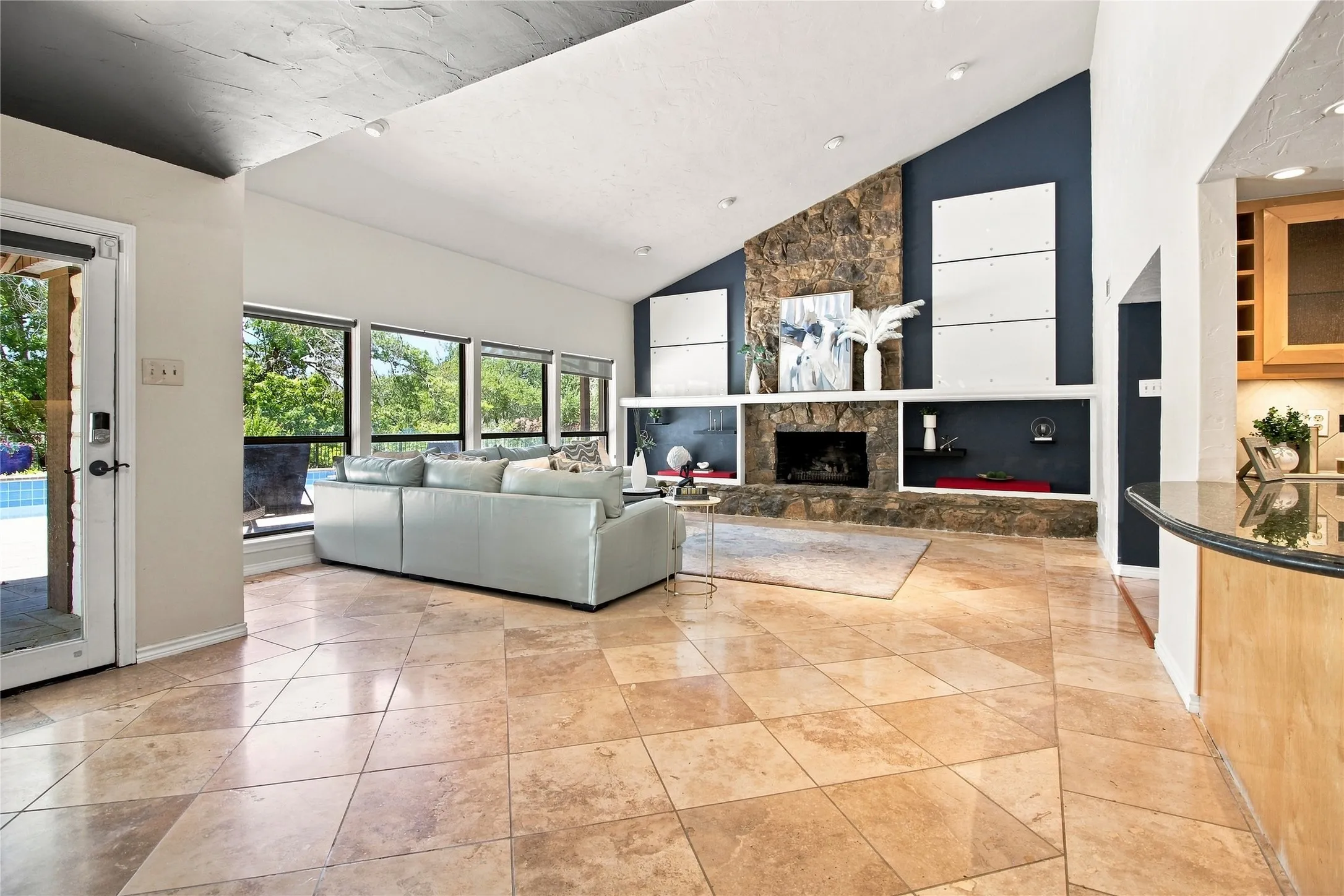 Vaulted ceilings, a stone fireplace, large pane windows, and tiled flooring