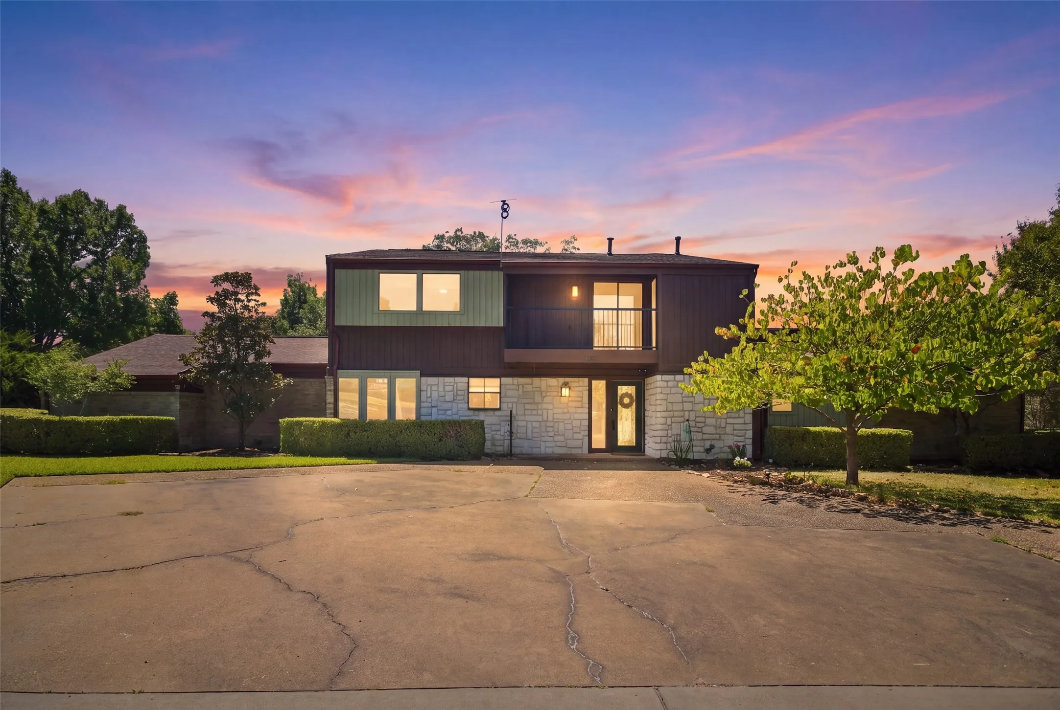 Multi-level exterior with stone and siding accents, featuring a second-story balcony with metal railing, a prominent front entry, and a paved driveway