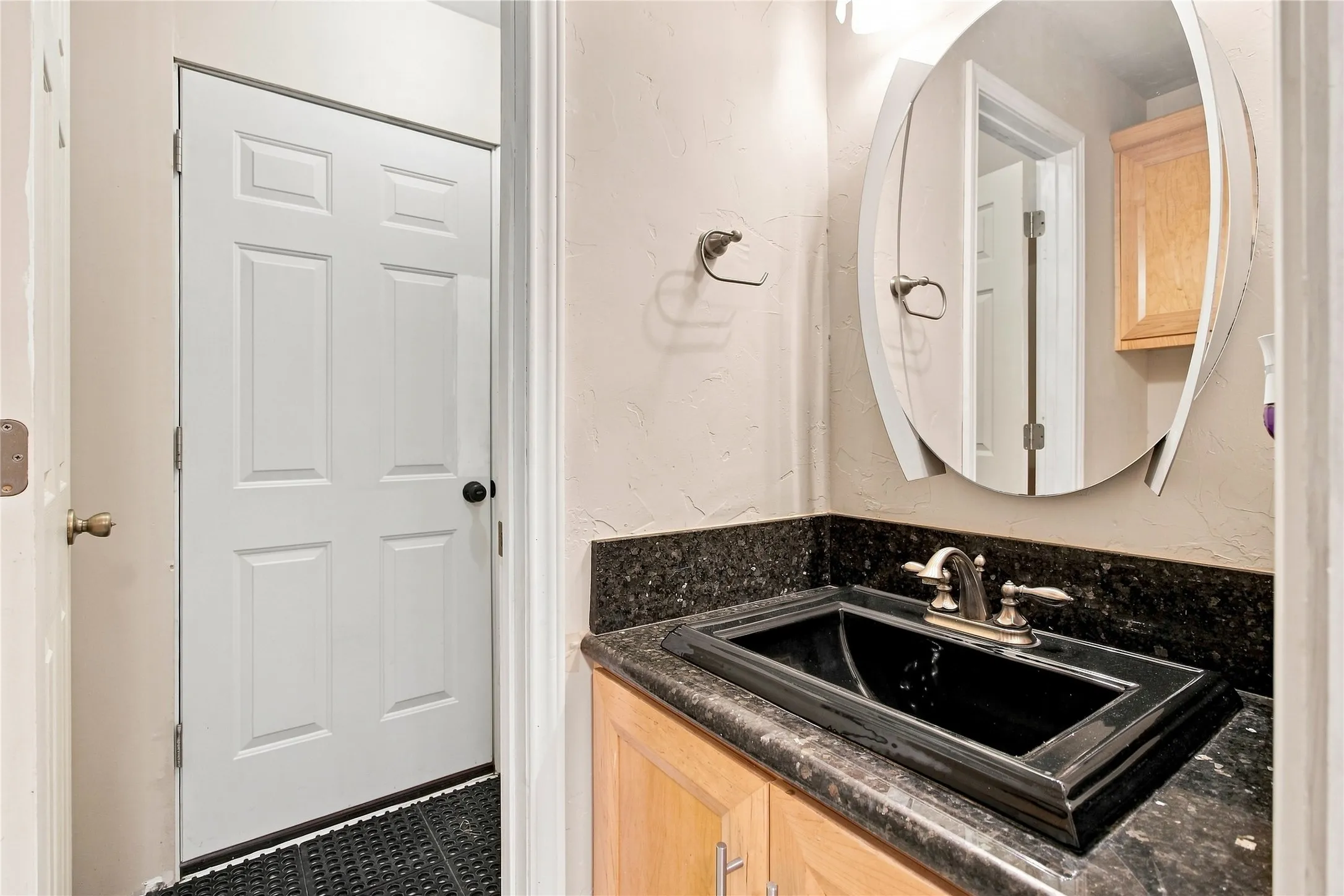 Half bathroom with black rectangular undermount sink with a two-handle faucet, set into a dark stone countertop with a matching backsplash