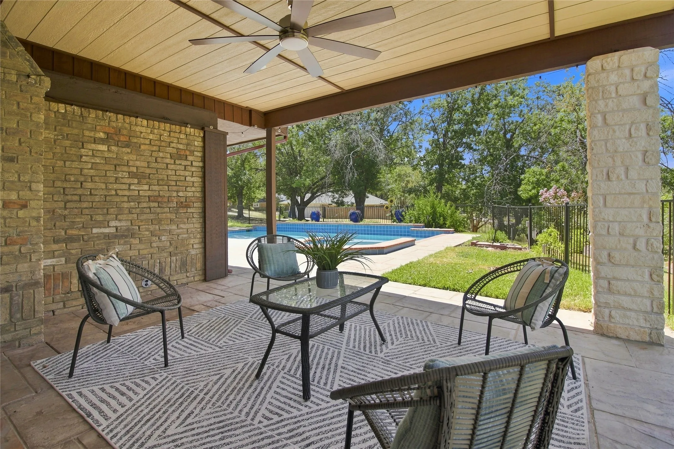 Covered patio with a ceiling fan, brick wall, stone column, and a swimming pool
