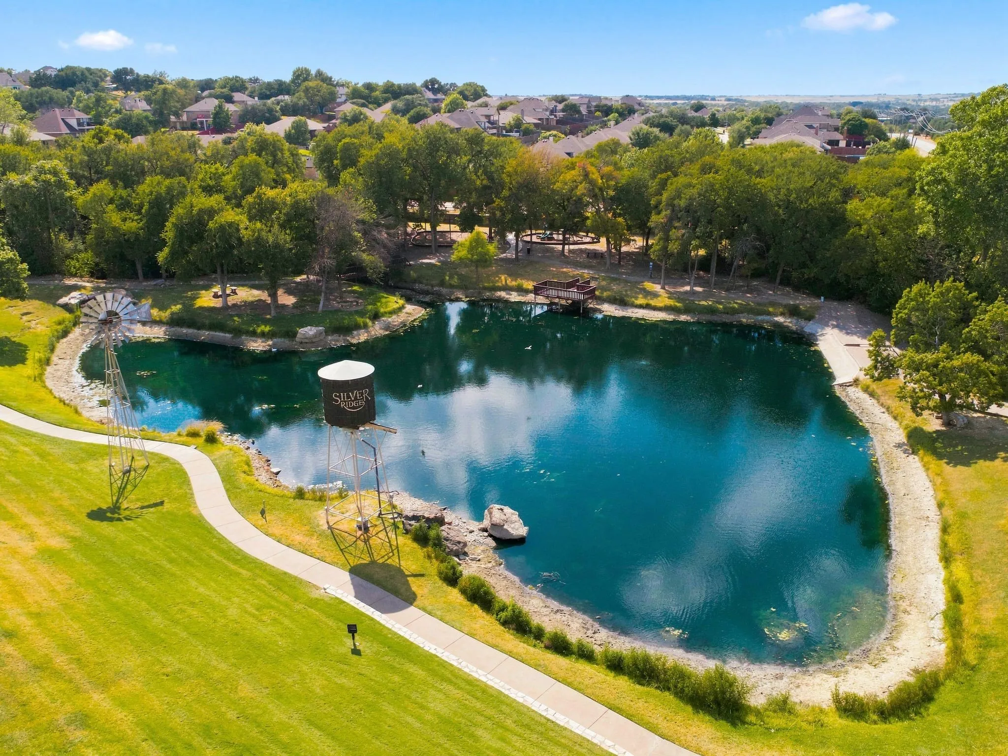 Expansive water feature with surrounding green space, mature trees, a winding pathway at the entrance to the neighborhood