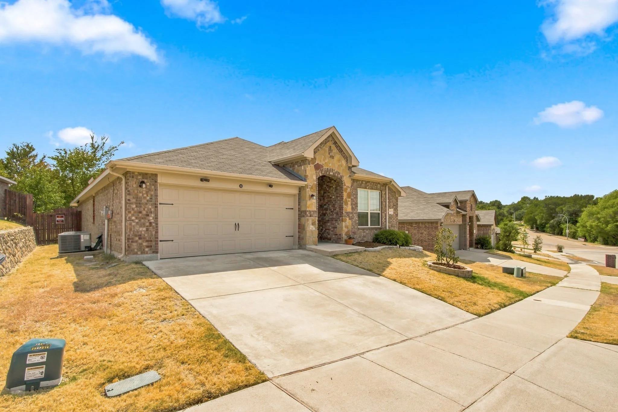Brick and stone exterior with an attached two-car garage, concrete driveway, and a sidewalk