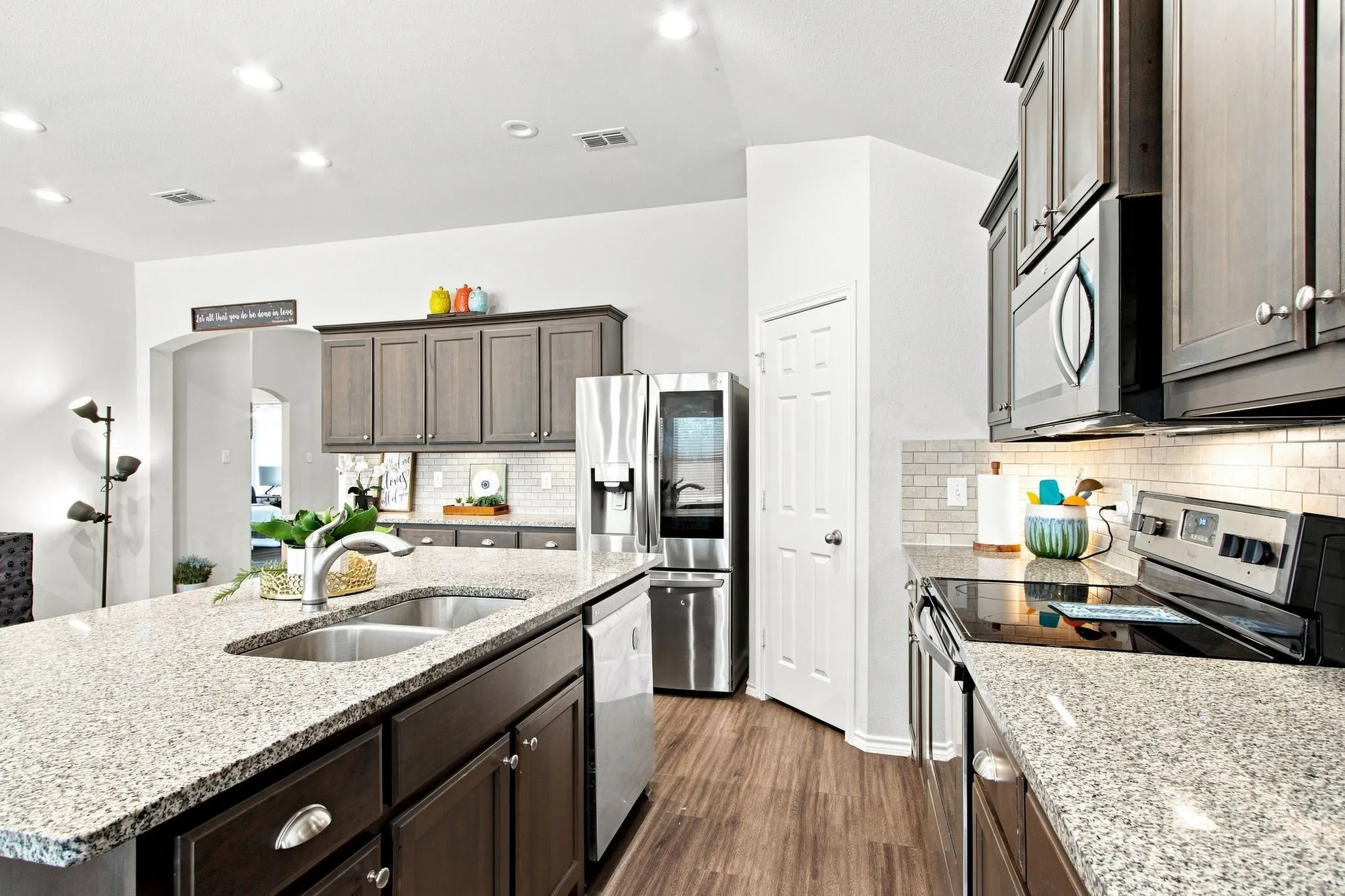 Kitchen featuring a large island with a double basin sink, stainless steel appliances, wood-finish LVP flooring, recessed lighting, and a walk in pantry