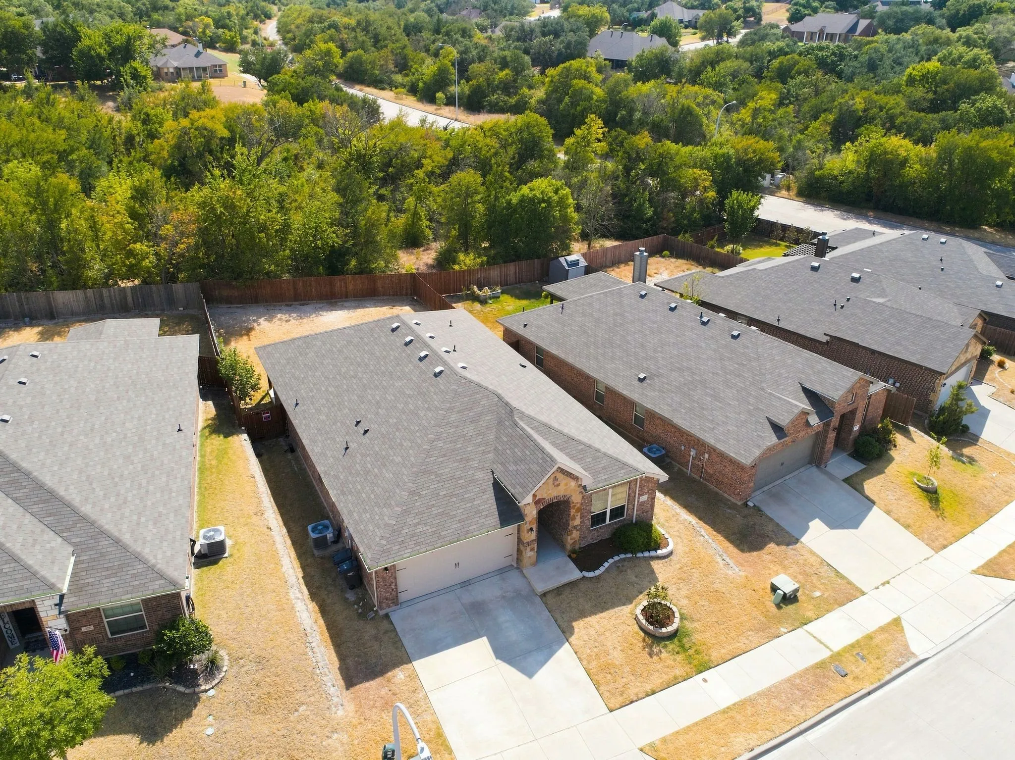 Brick and stone exterior with an attached garage, paved driveway, and lovely treed greenspace behind the property
