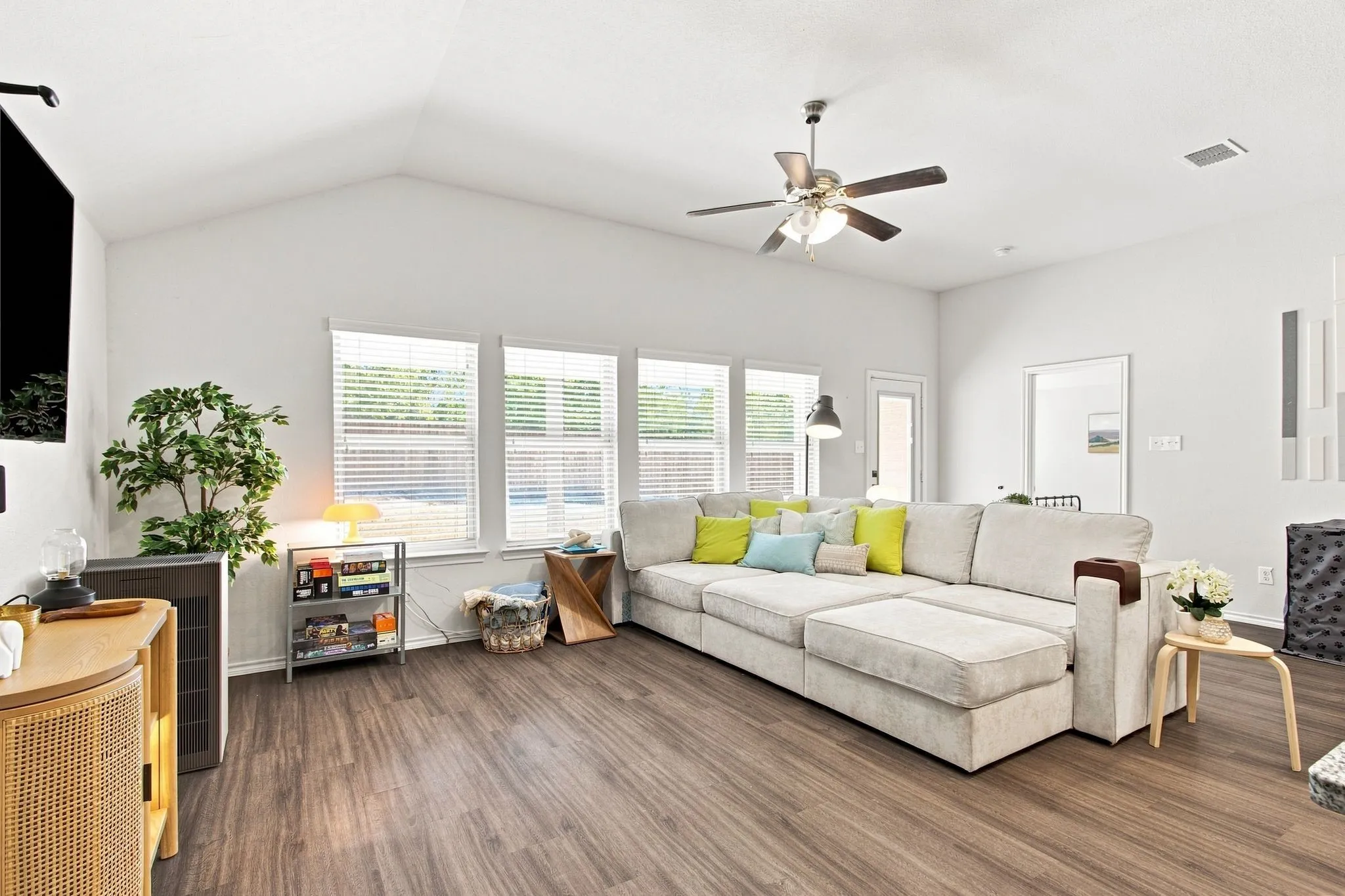 Vaulted ceiling with a ceiling fan, wall of windows with blinds, wood-finish LVP flooring, and white walls
