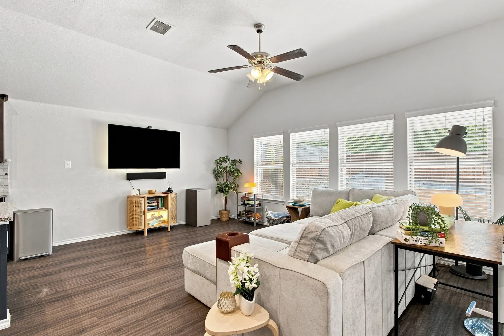 Vaulted ceiling with a ceiling fan, multiple windows with blinds, and wood-finish LVP flooring