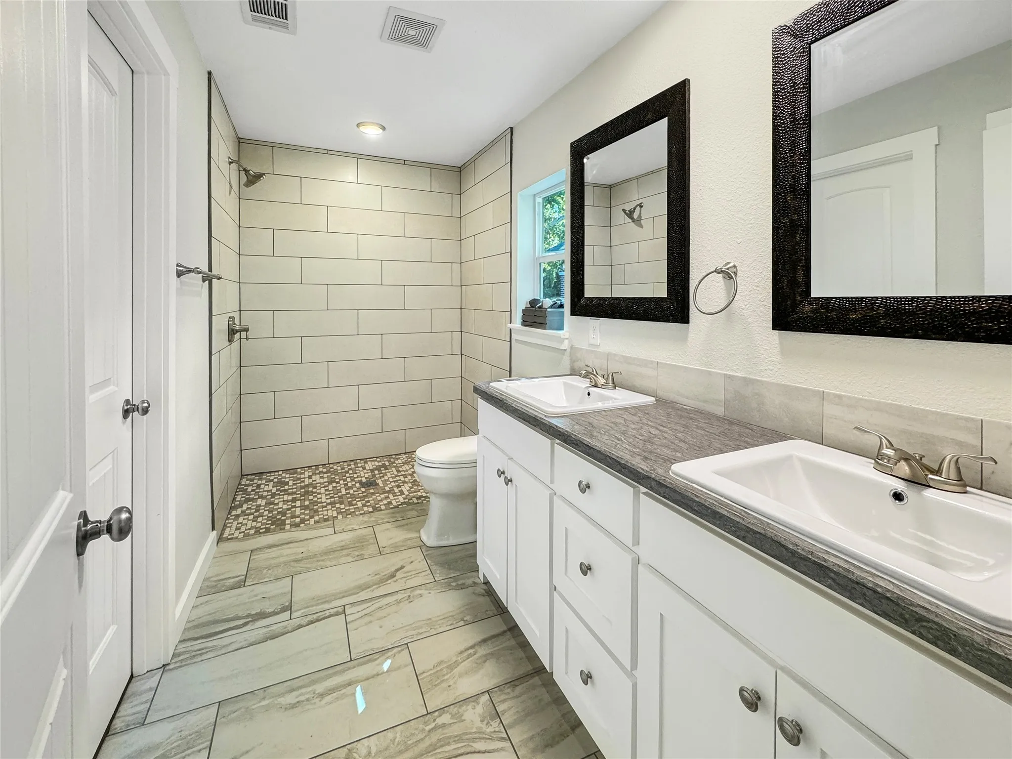 Dual undermount sinks, white cabinetry, dark countertops, and wheel chair accessible shower