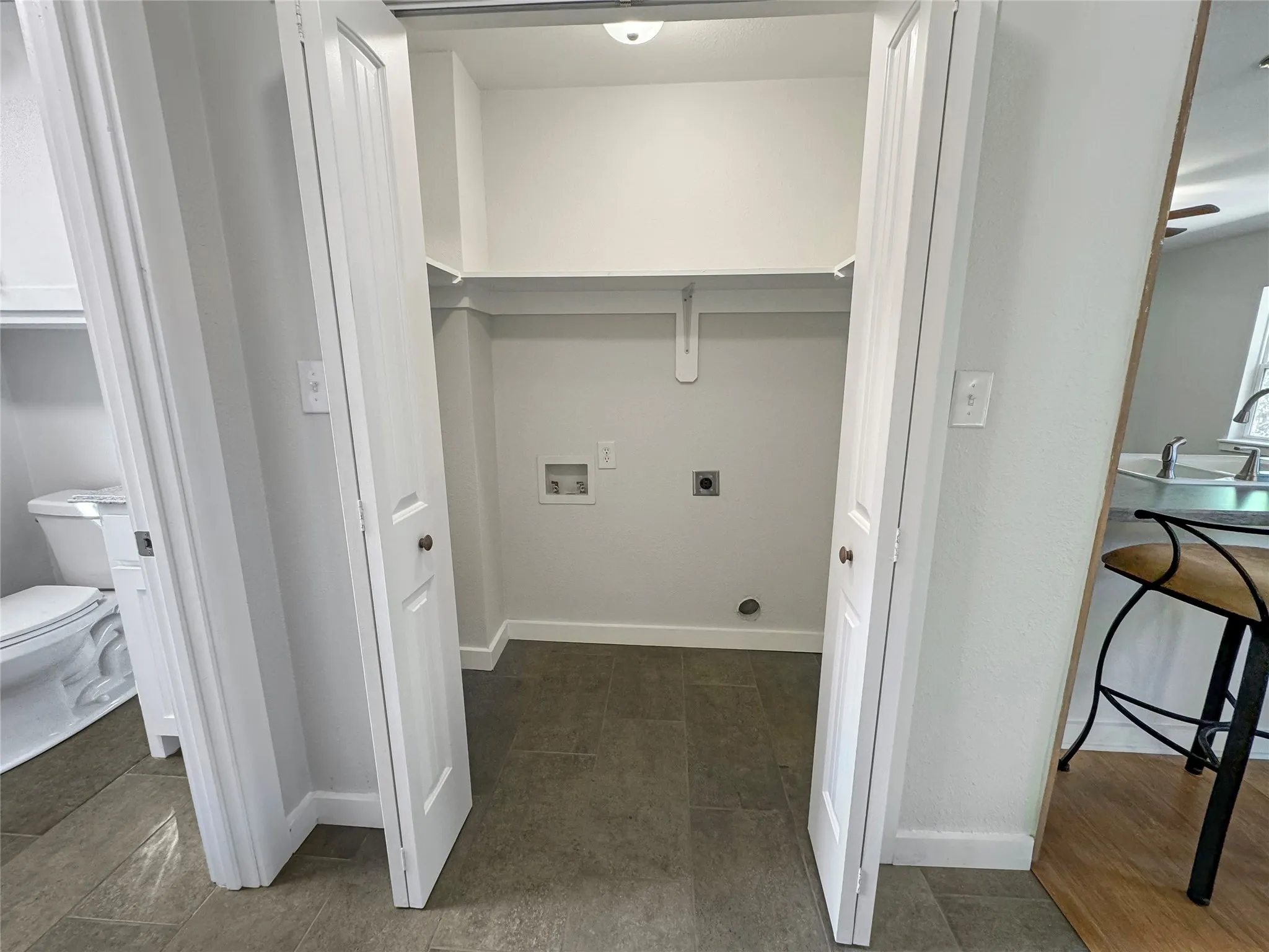 Compact laundry area with bi-fold doors, overhead shelving, and tile flooring