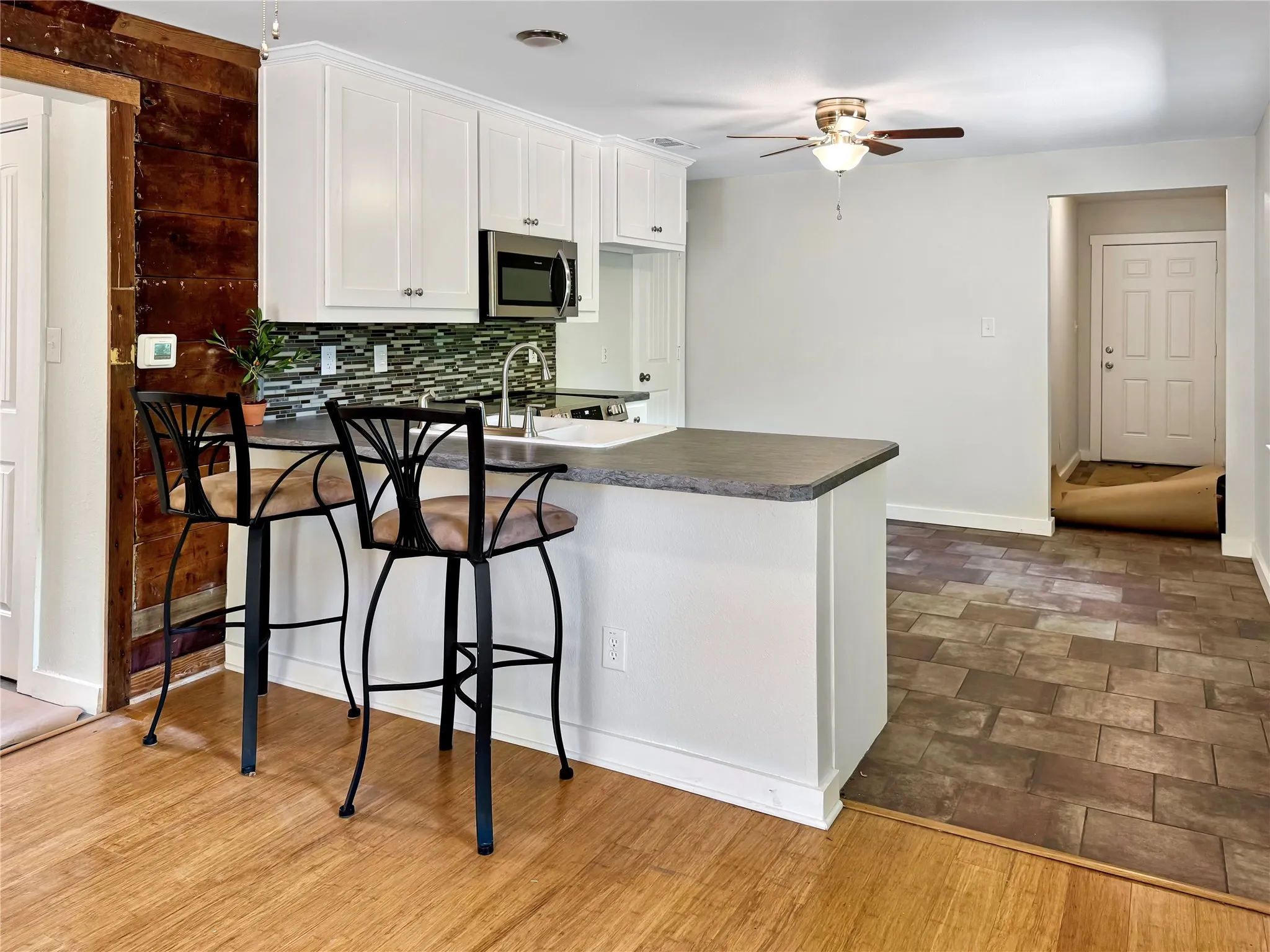 White upper cabinetry with stainless steel hardware, stainless steel microwave, and glass mosaic tile backsplash