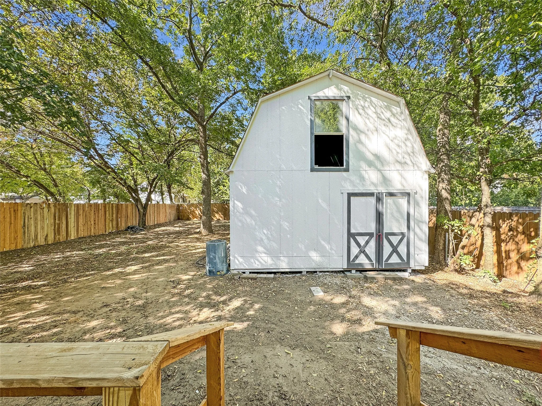 Detached Two-Story Barn/Workshop  in Fenced Backyard featuring double barn doors and an upper floored loft, surrounded by mature trees and a wood privacy fence