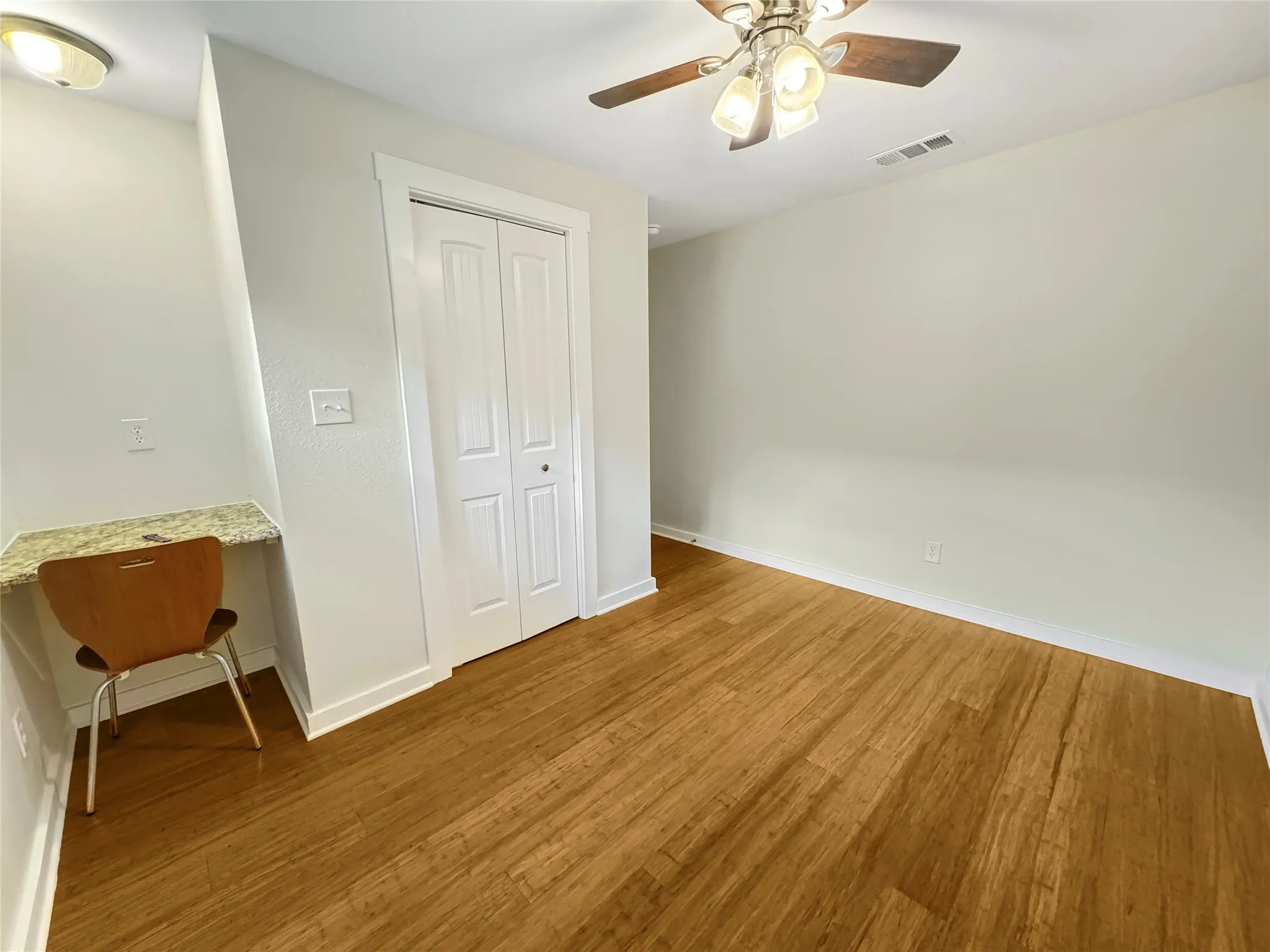 Secondary Bedroom - Bamboo flooring, built-in corner desk with a granite countertop, ceiling fan with integrated lighting, and a bi-fold closet door
