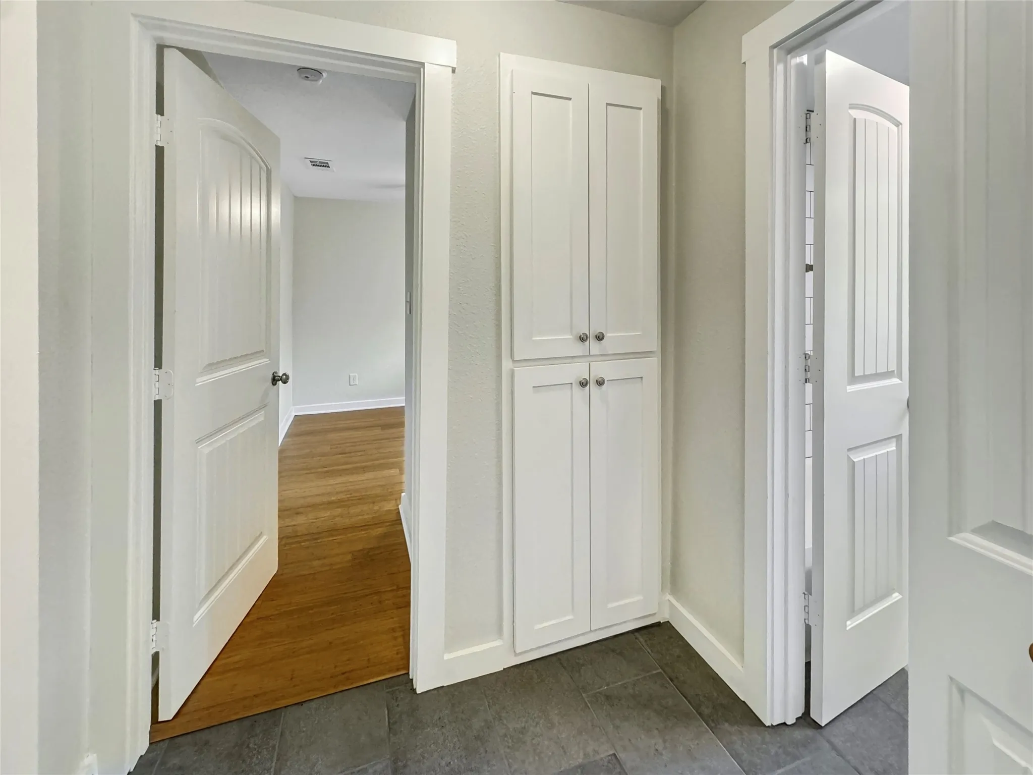Bright hallway showcasing white built-in cabinetry with double doors and brushed nickel hardware, and neutral wall finishes throughout
