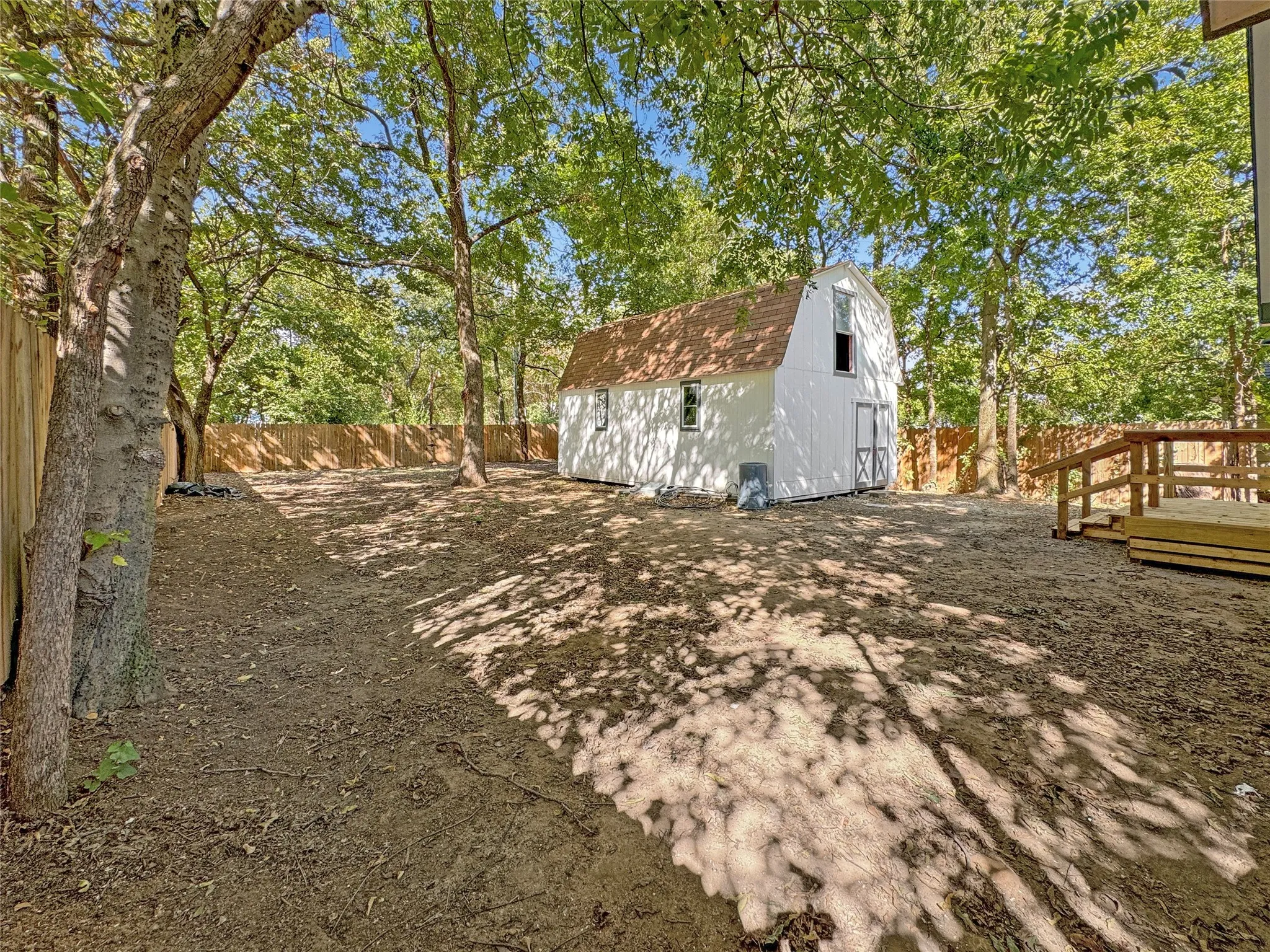 Expansive yard with mature trees, a privacy fence, a white barn-style outbuilding/barn, and a wood deck with railings