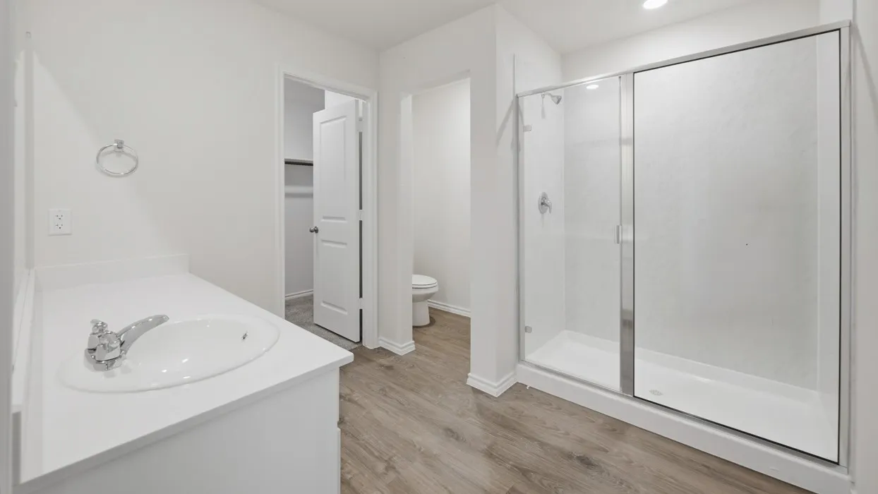 Contemporary bathroom featuring a spacious glass-enclosed shower, white vanity with integrated sink, chrome fixtures, recessed lighting, and wood-finish flooring