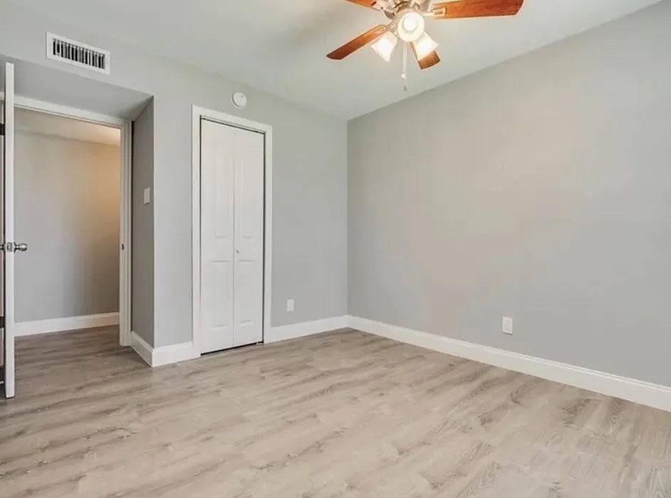 Wood-finish flooring, light gray wall paint, white baseboards, bi-fold closet doors, and a ceiling fan