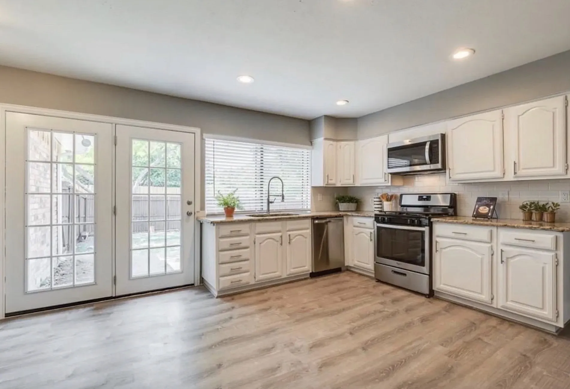 White cabinetry with brushed nickel hardware, stainless steel appliances, granite-style countertops, wood-finish flooring, and French patio doors