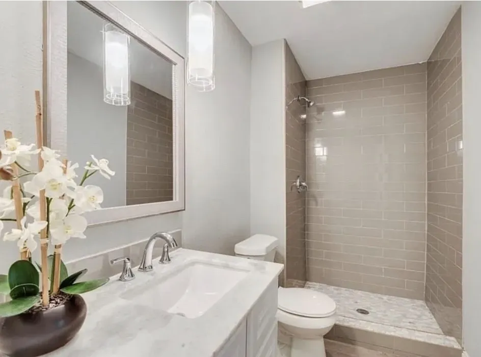 Vanity with chrome fixtures and a white countertop, framed mirror, two pendant light fixtures, and a shower with subway tile surround and a tiled floor
