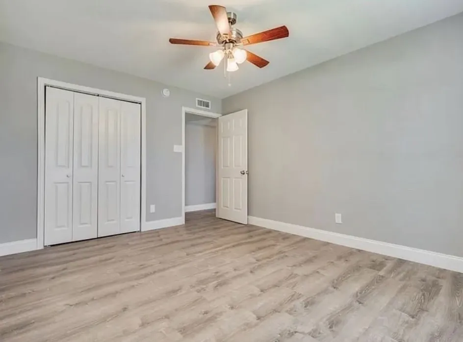 Wood-finish flooring, light grey wall paint, bi-fold closet doors, ceiling fan with light fixture, and white trim