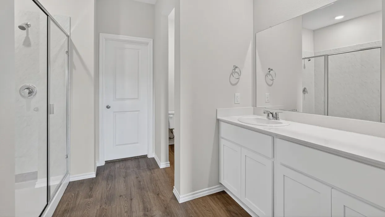Bathroom featuring a glass-enclosed shower, wood-finish flooring, white vanity with integrated sink, and an expansive wall mirror