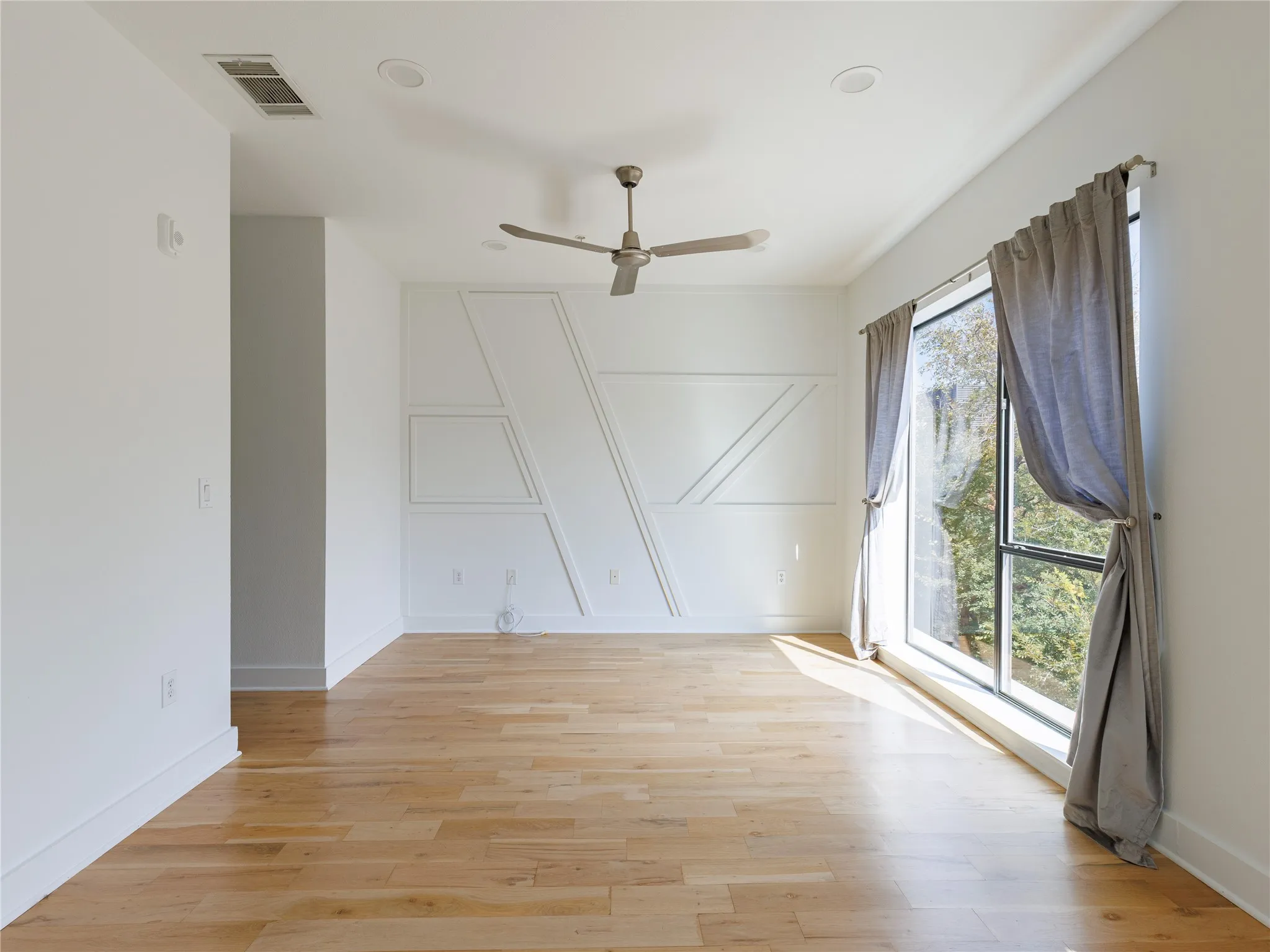 Light-filled bedroom featuring hardwood floors, a ceiling fan, and peaceful views of the surrounding trees.