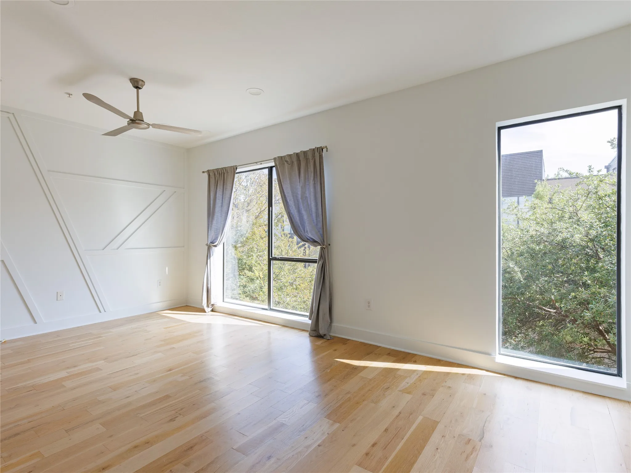 Spacious bedroom with hardwood flooring, high ceilings, oversized windows, and abundant natural light.