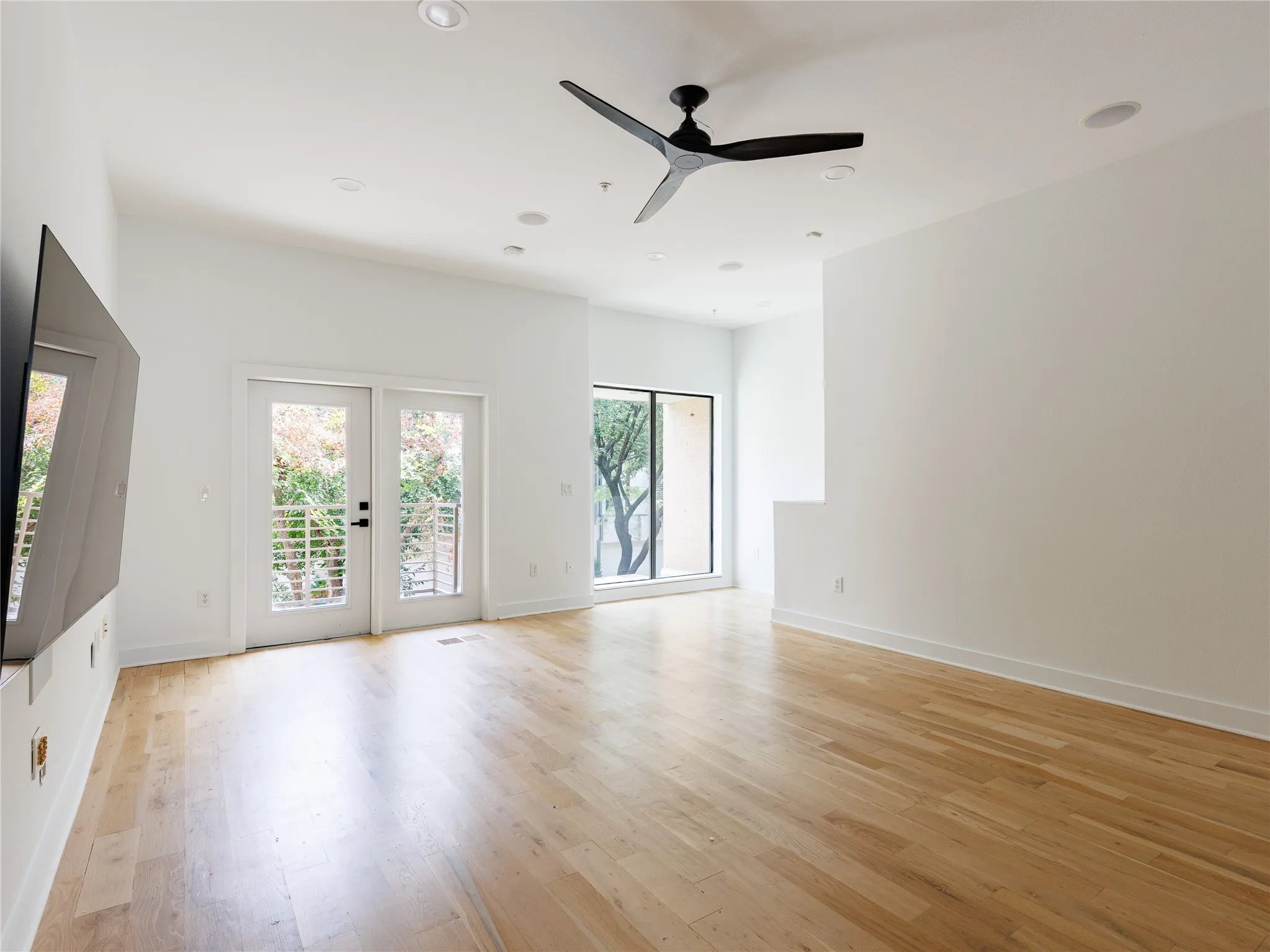 Expansive living room with hardwood floors, built-in speakers, recessed lighting, and balcony access.