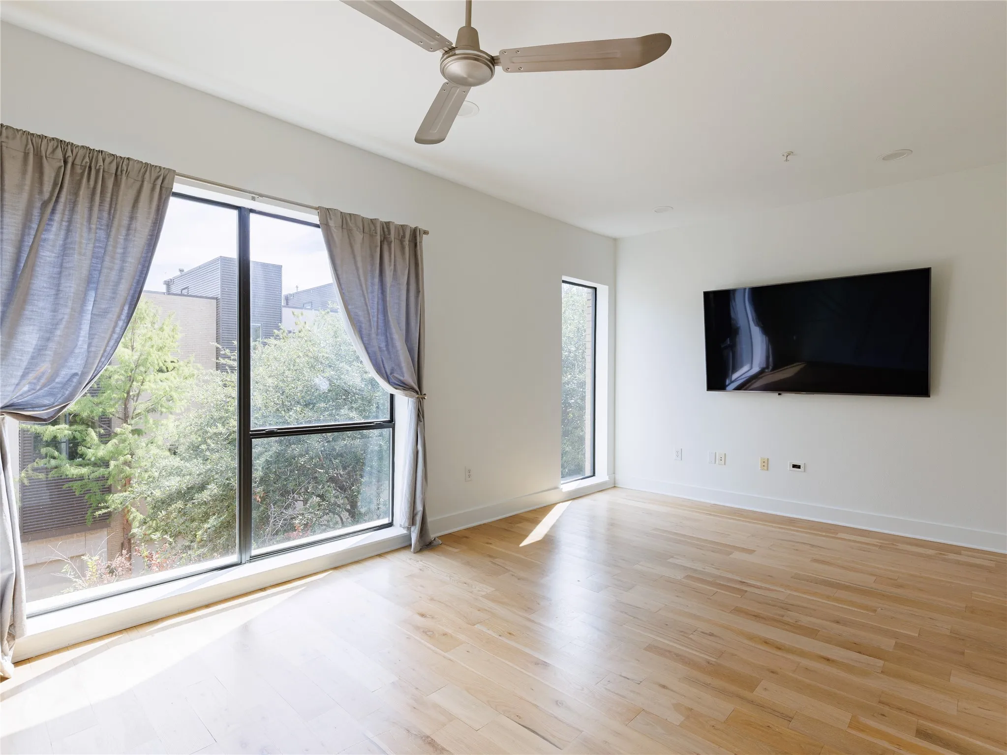Spacious bedroom with hardwood flooring, high ceilings, oversized windows, abundant natural light, and peaceful treetop views.