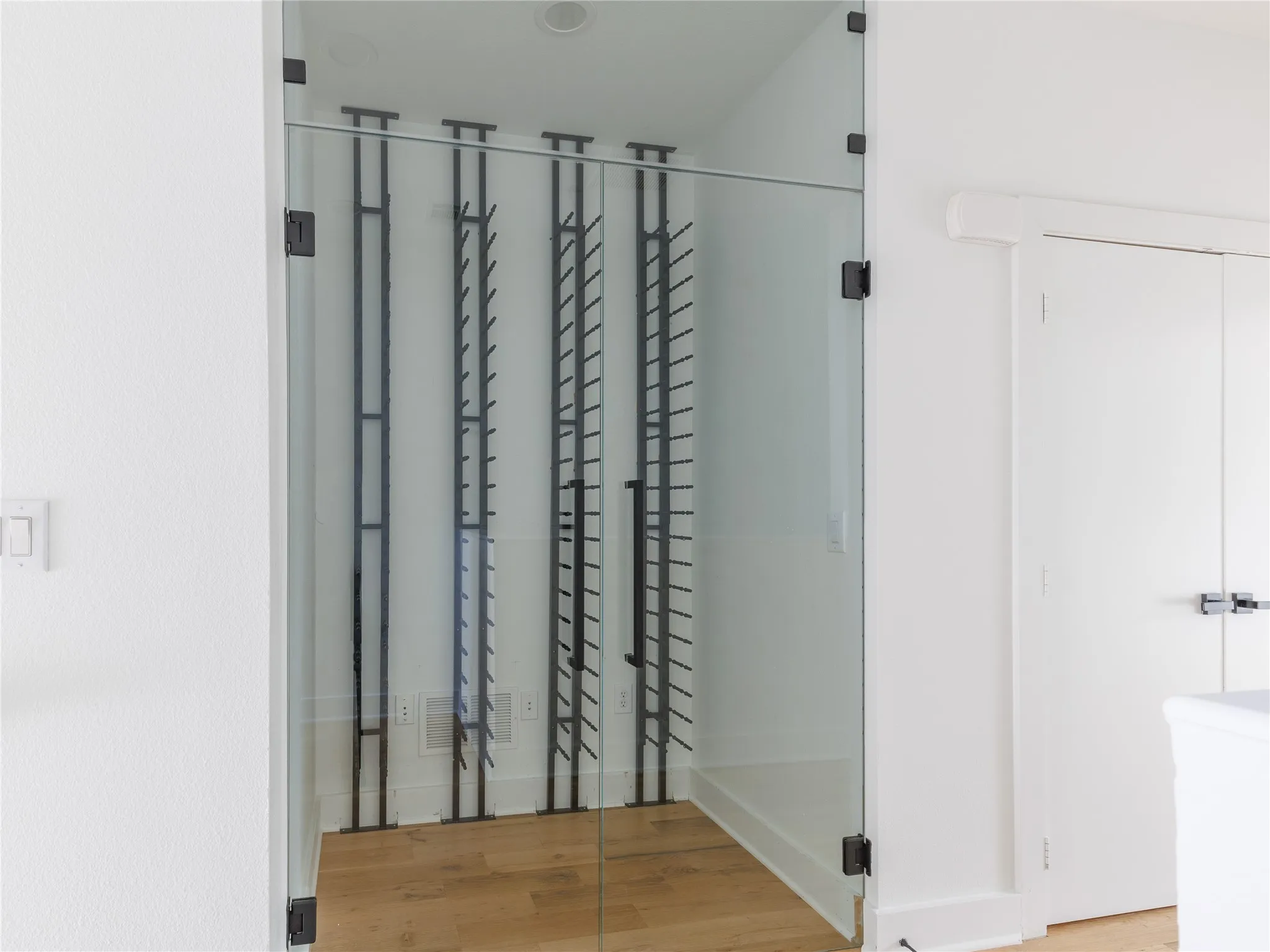 Glass-enclosed wine room featuring floor-to-ceiling bottle storage and modern matte black hardware.