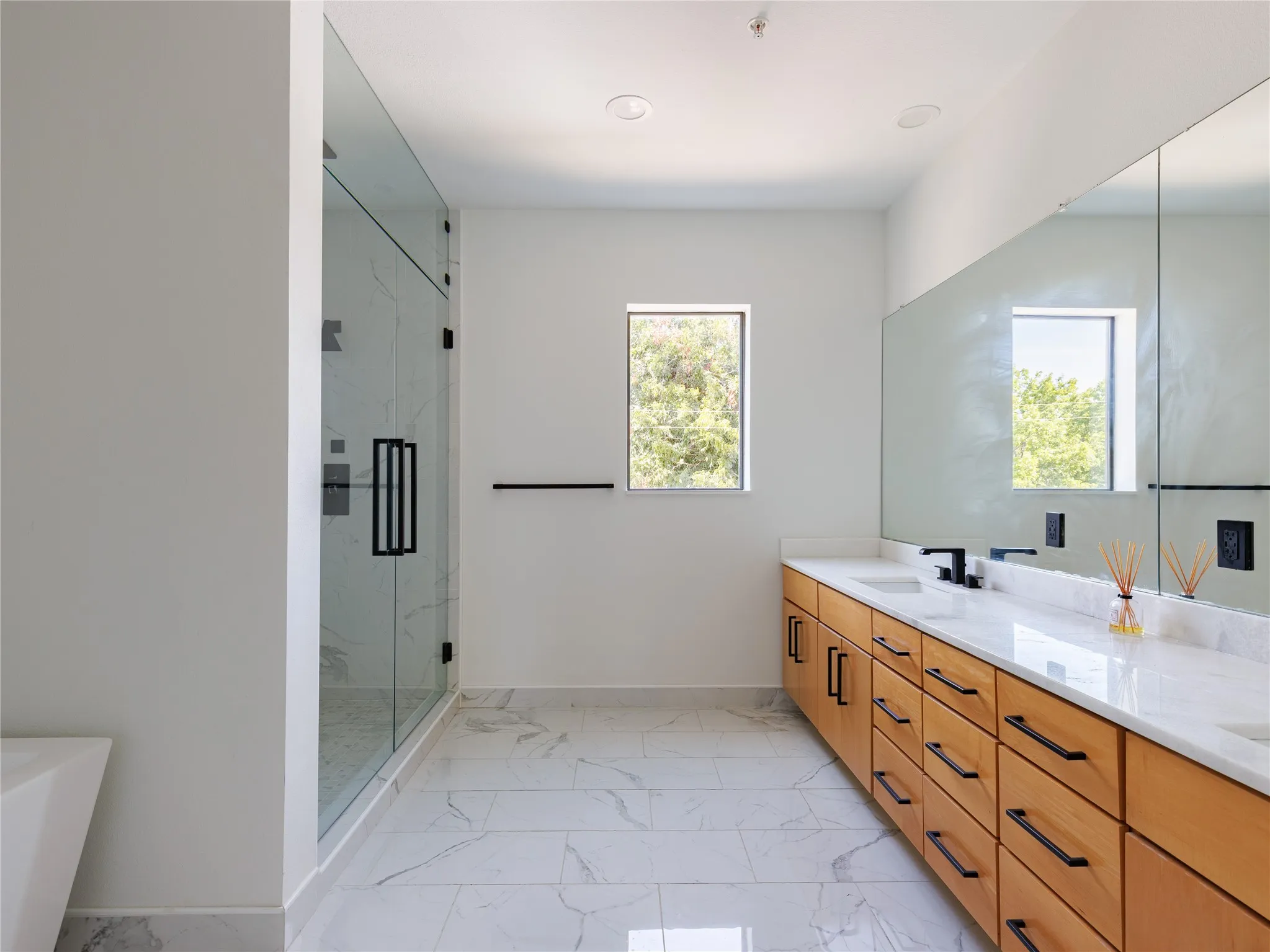 Spacious primary bathroom combines a freestanding tub, large walk-in shower, marble counters, and porcelain tile floors.