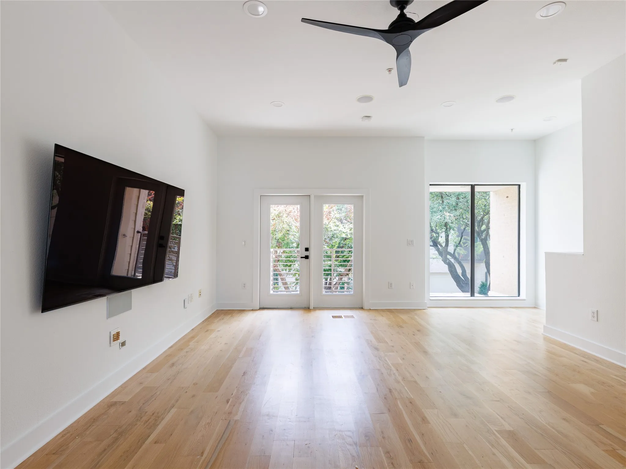 Open living room with hardwood flooring, tall ceilings, oversized windows, and balcony access.