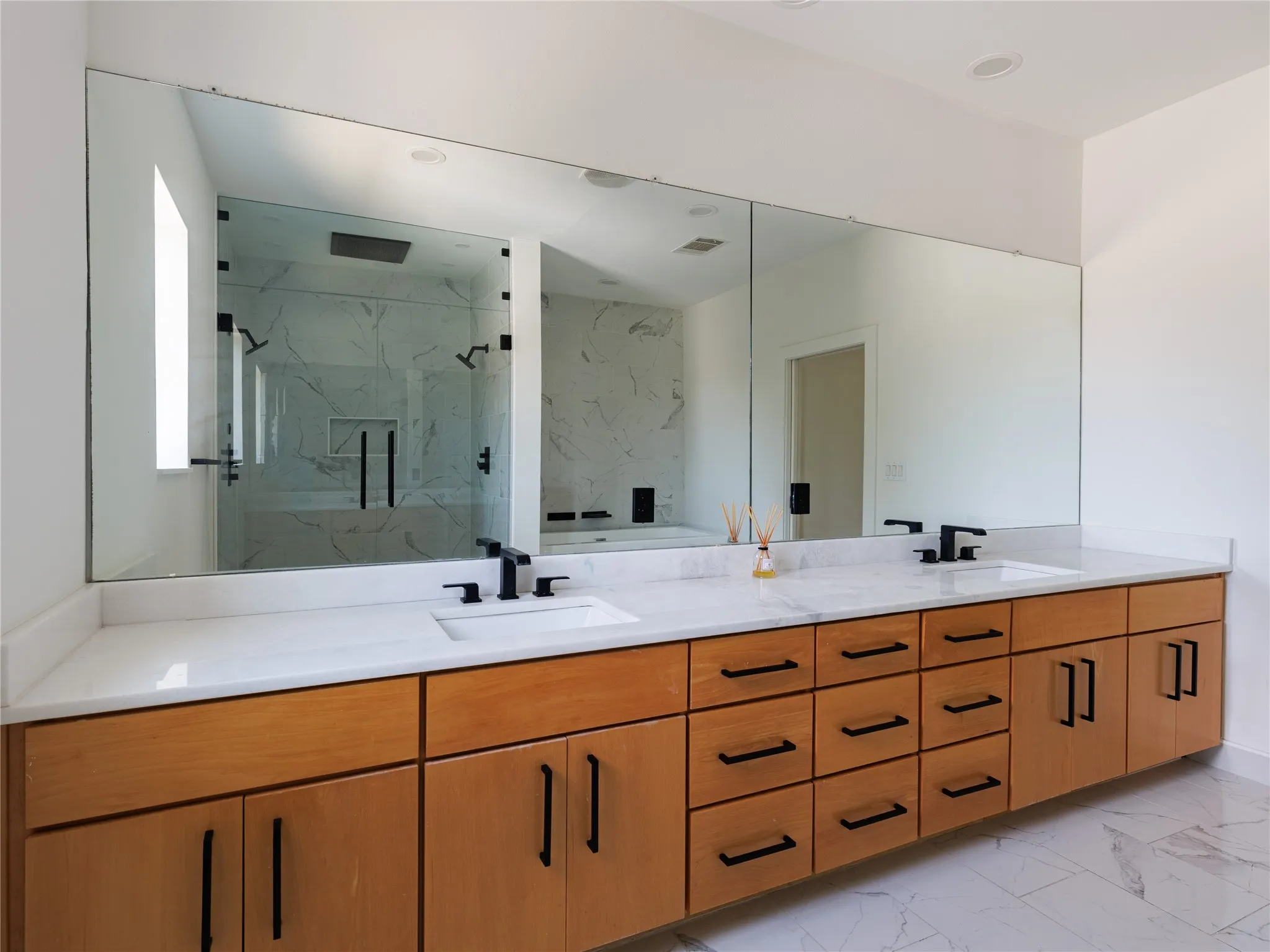 Light-filled primary bathroom featuring a freestanding soaking tub, oversized walk-in shower, marble countertops, and porcelain tile floors.